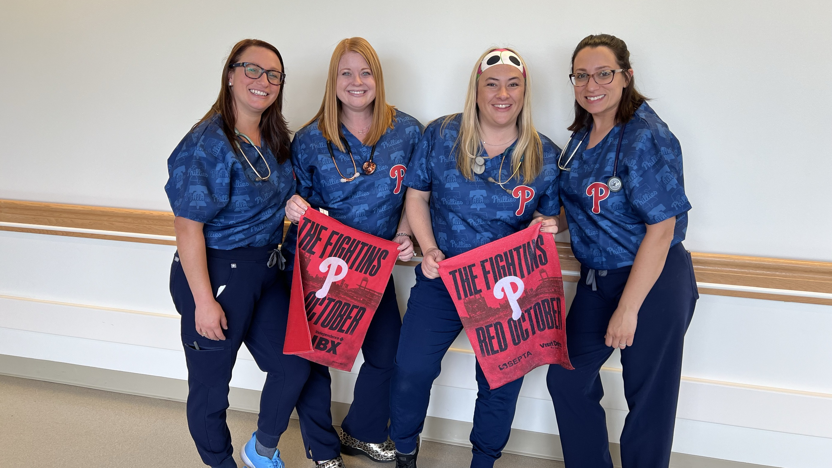 A group of hospital staff wearing blue Phillies shirts holding a Phillies pennant