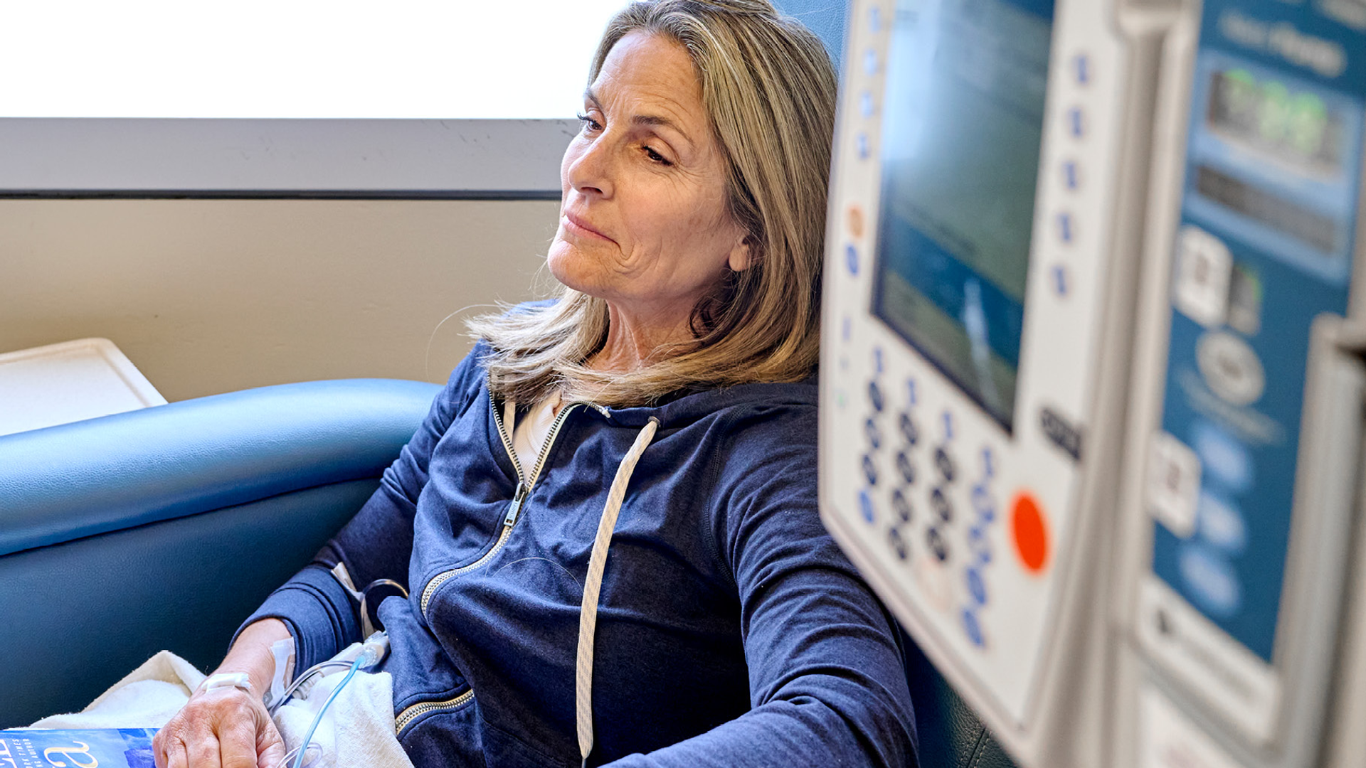 Amy Darragh sits in an infusion chair receiving chemotherapy, a book on her lap