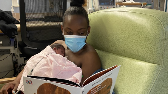With her baby laying on her chest, a mother sits in the nursery reading from the book, Brown Bear, Brown Bear, What Do You See?