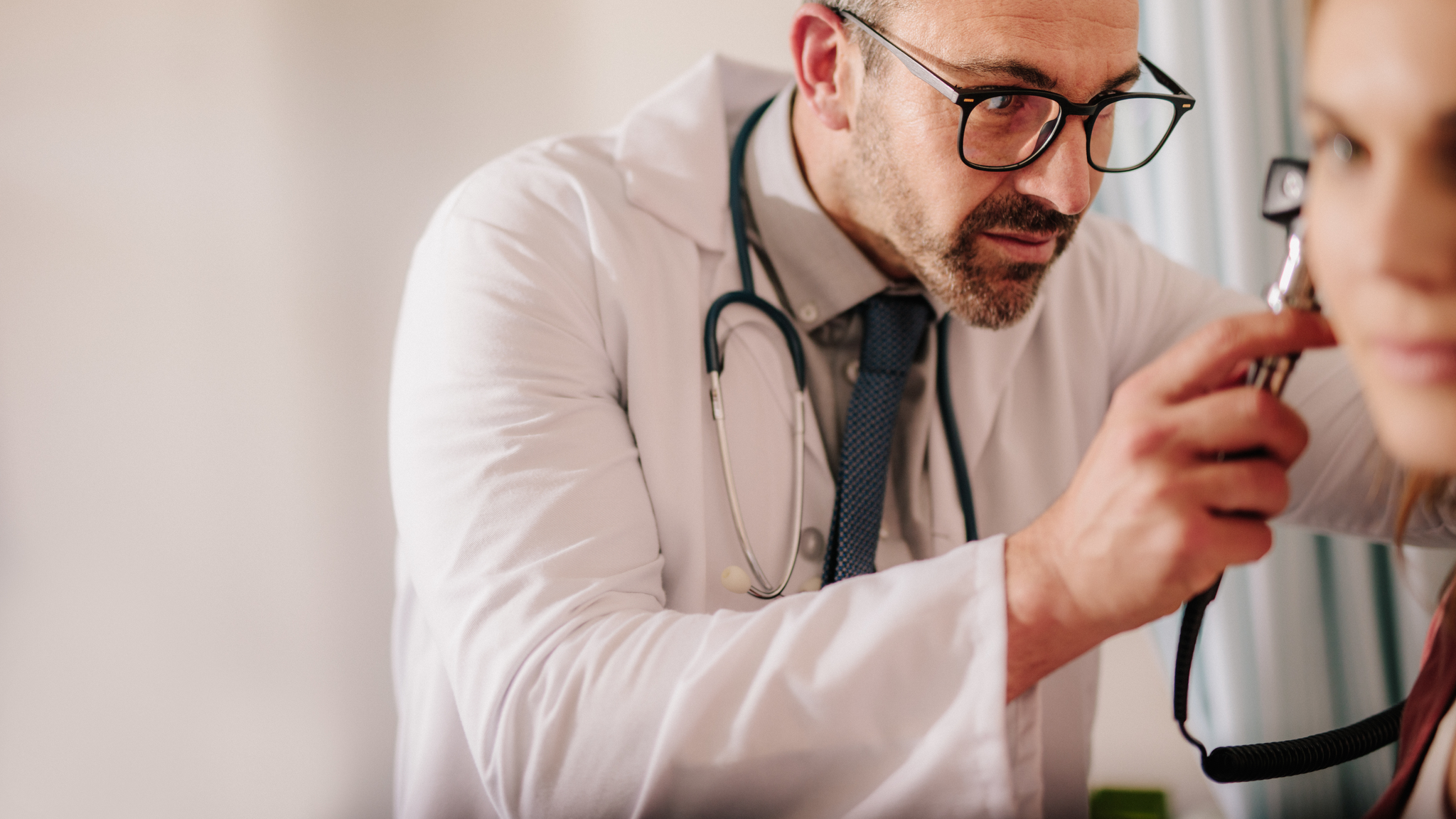Male doctor looking at female patient's ear through otoscope