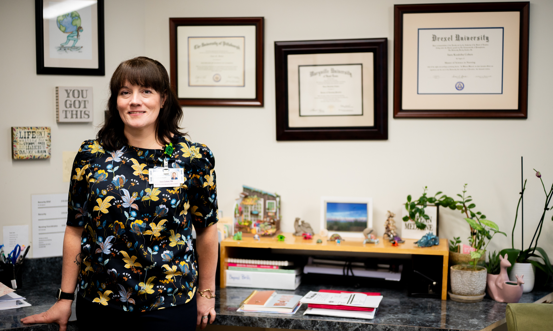 Sara Cohen standing in her office in front of a wall with three framed college degrees