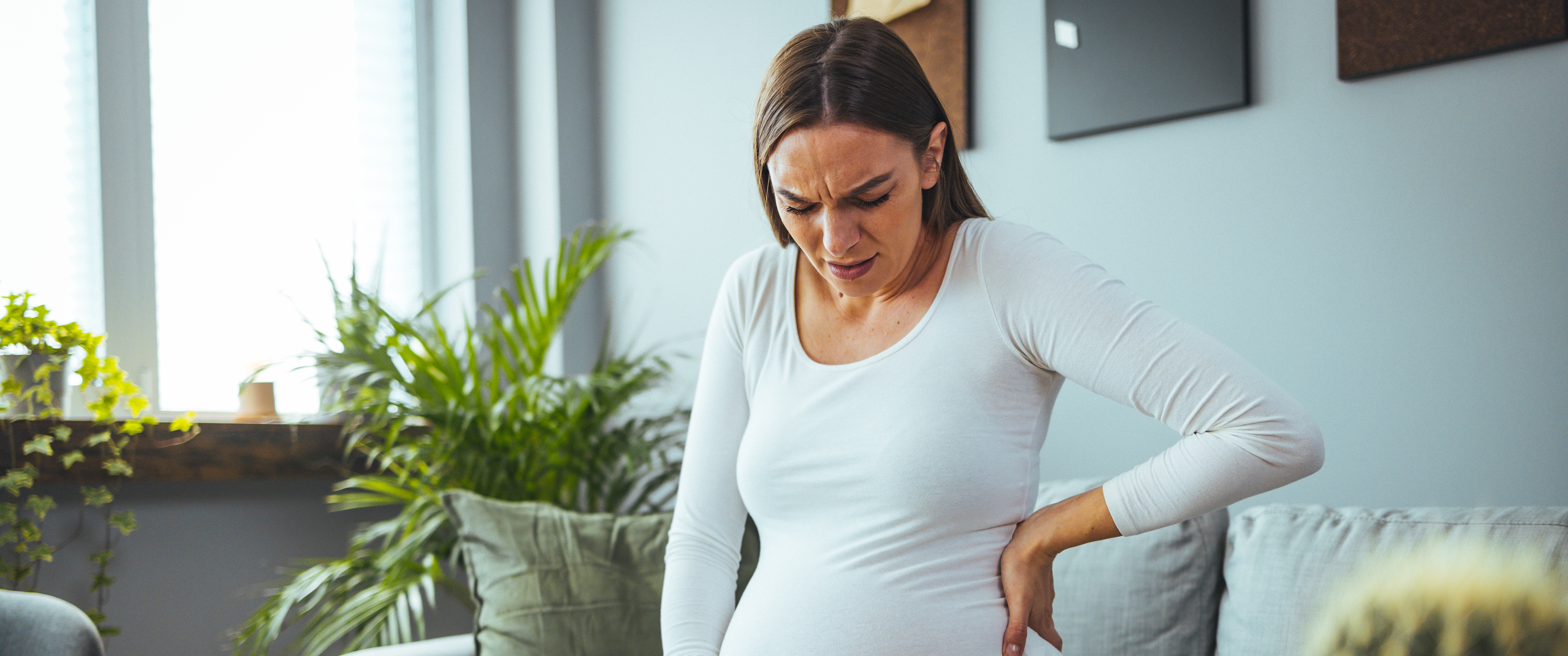 Pregnant woman feeling pain while working in the office, her hands touch her stomach and back