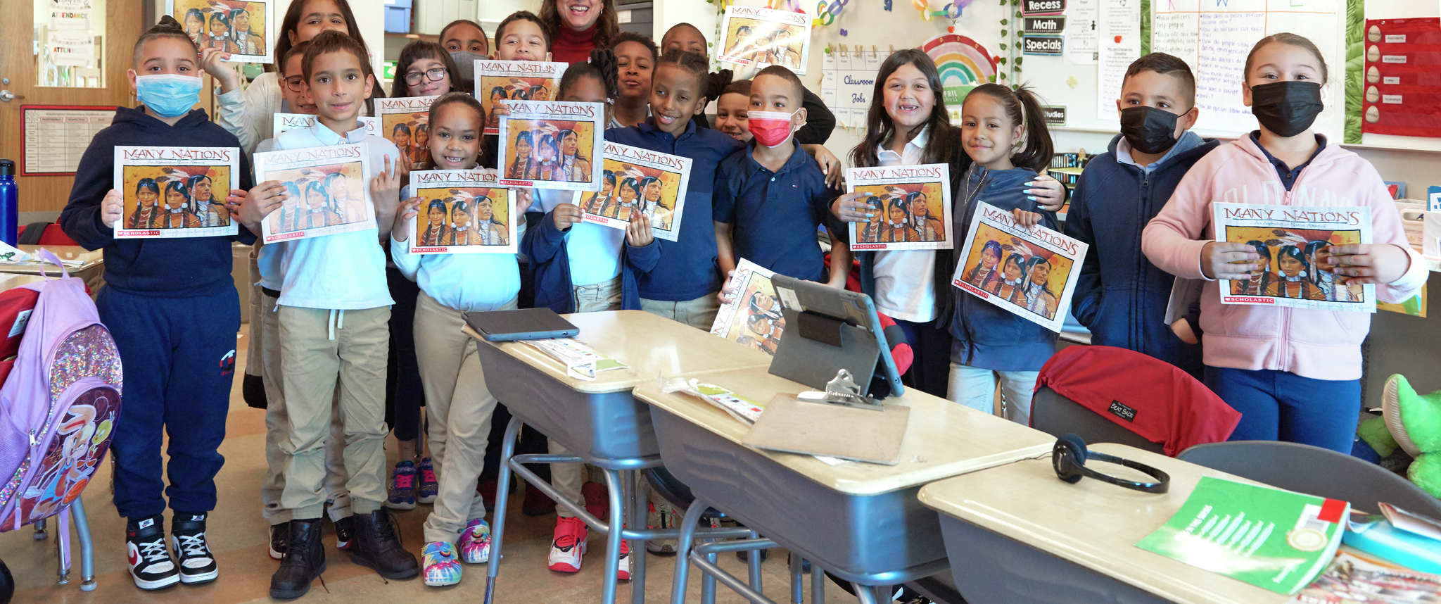 Group photo of children in a classroom holding up books with Evelin La Paz in the background