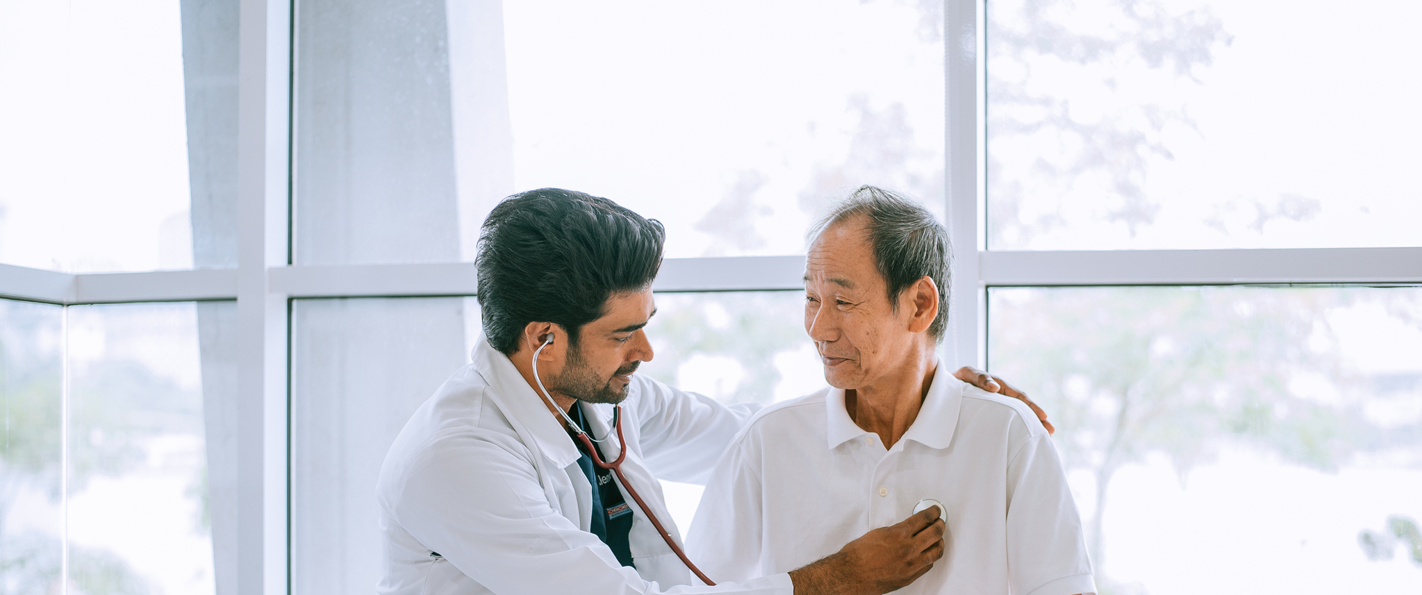 Doctor and patient in an exam room, doctor listens to the patient's heart