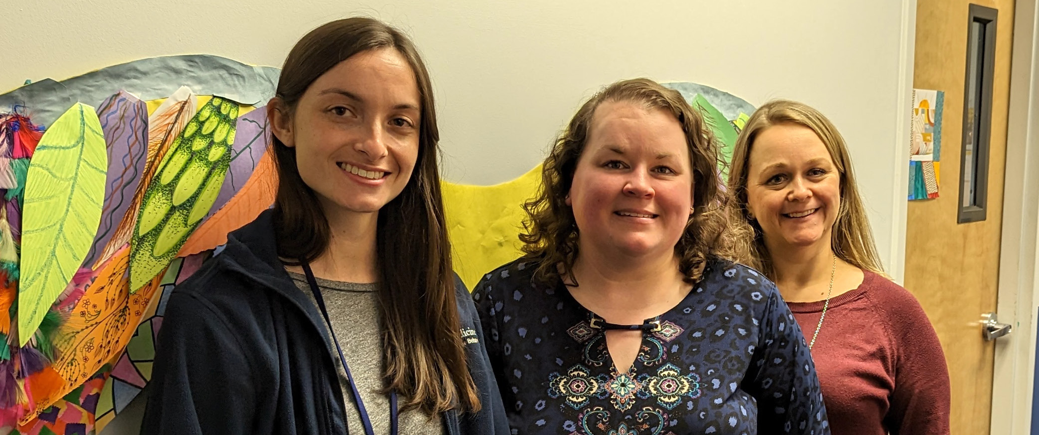 Danielle Andersen, Jacqueline Pidich, and Jamie Benjamin with artwork depicting wings