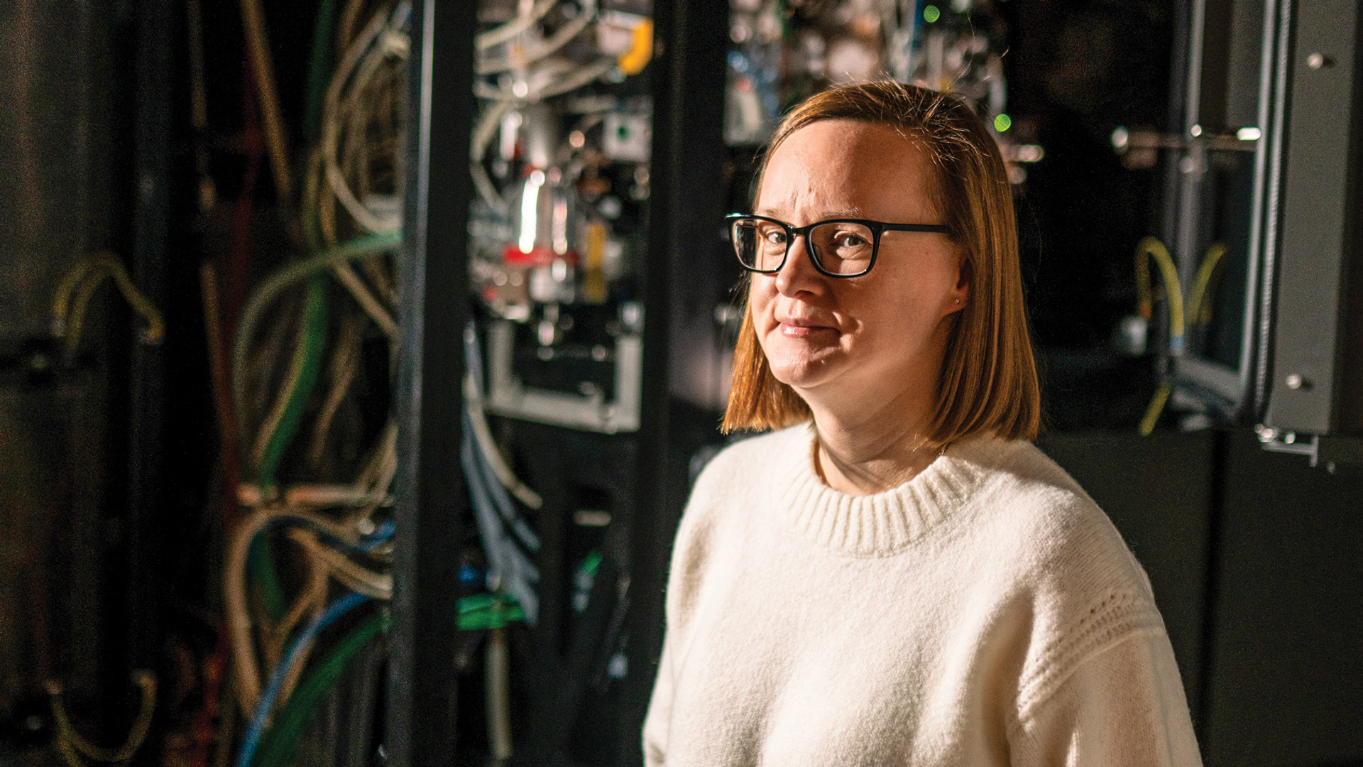 Vera Moiseenkova-Bell, PhD, stands in front of a large machine filled with wires—the electron microscope used for cryoEM studies