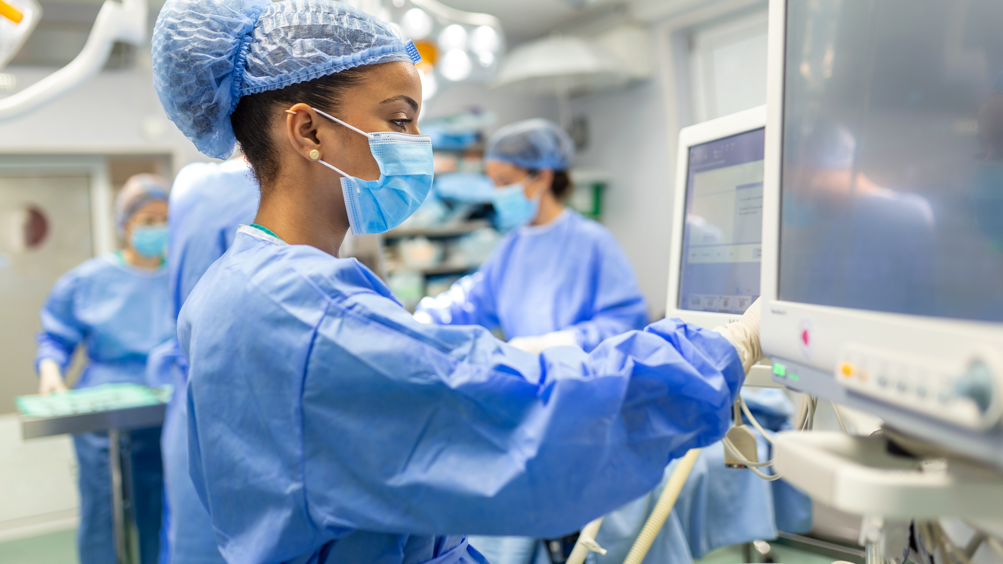 Provider checking monitors while sedating patient before surgical procedure in hospital operating room. 