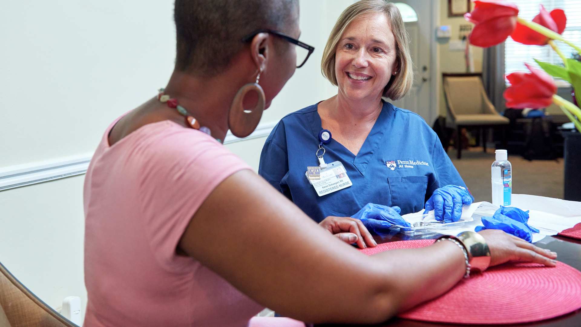 A home care nurse sits with a patient at her dining room table