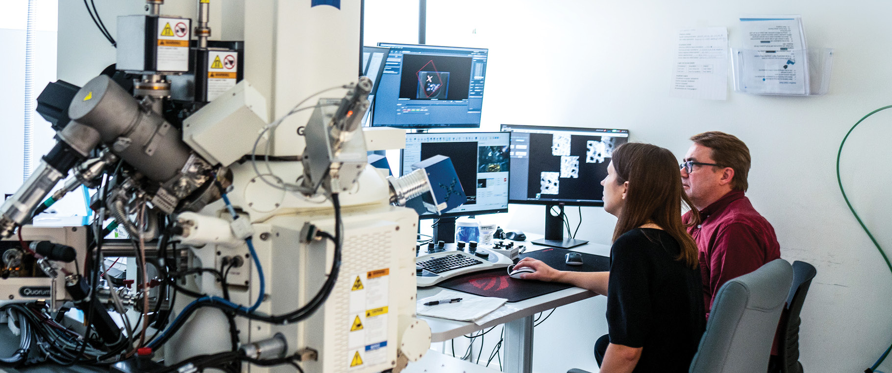Kathryn Kixmoeller and Ben Black sit in front of an array of multiple monitors, viewing molecular images