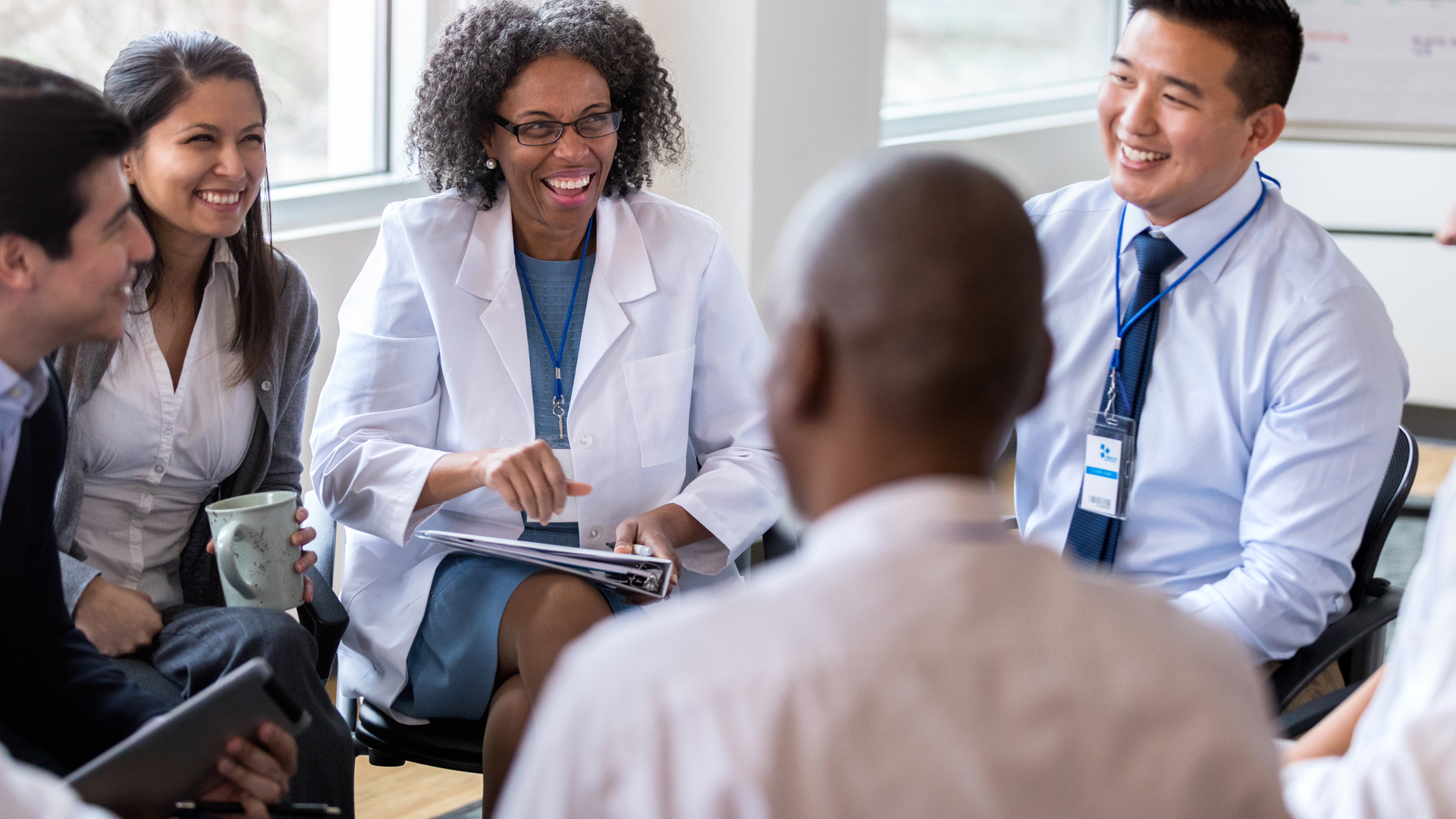 A group of cheerful medical coworkers sit in a circle for a staff meeting