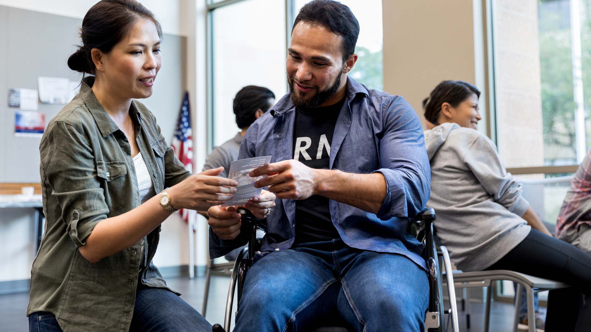 A woman shares an informational handout for veterans with an army vet in a wheelchair.