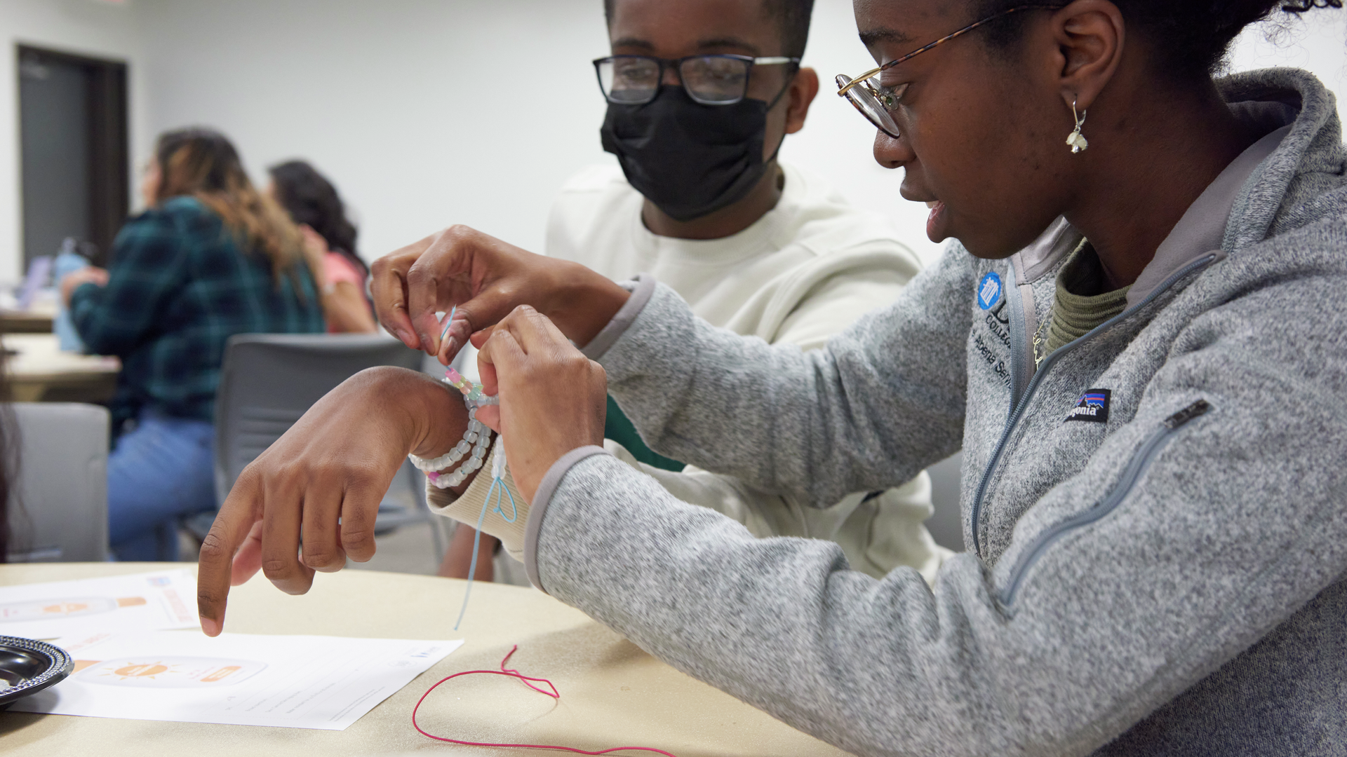 Michel Ntiri helps a male student put on a handmade bracelet