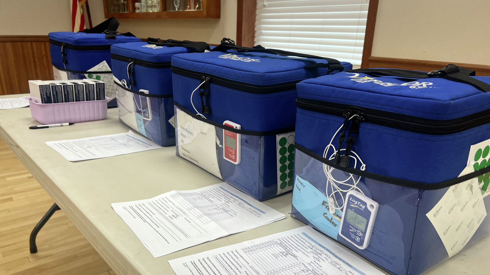 Blue containers holding vaccines, placed on a folding table within the fire hall vaccine clinic.
