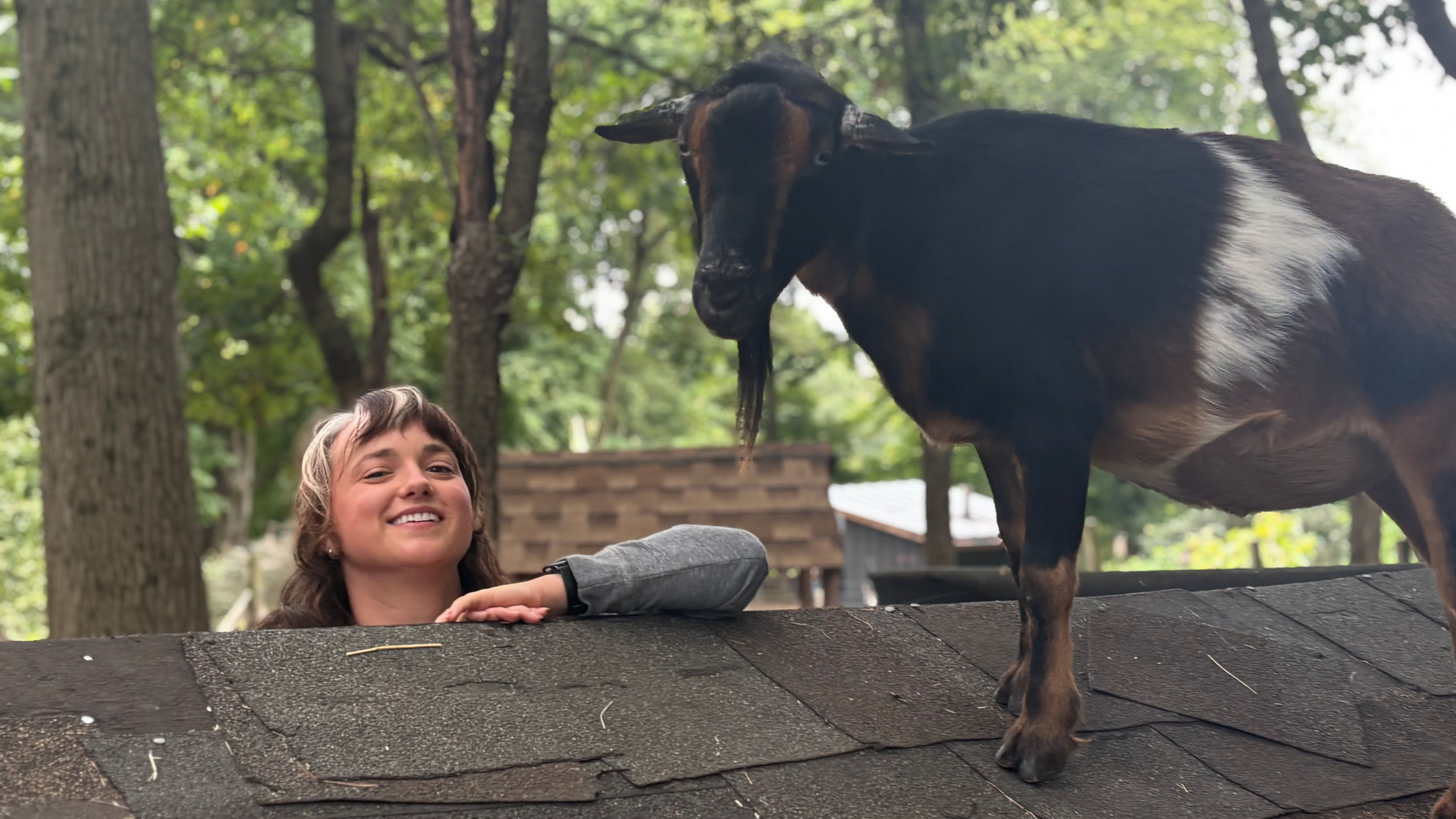 A smiling woman with a goat perched atop a rooftop