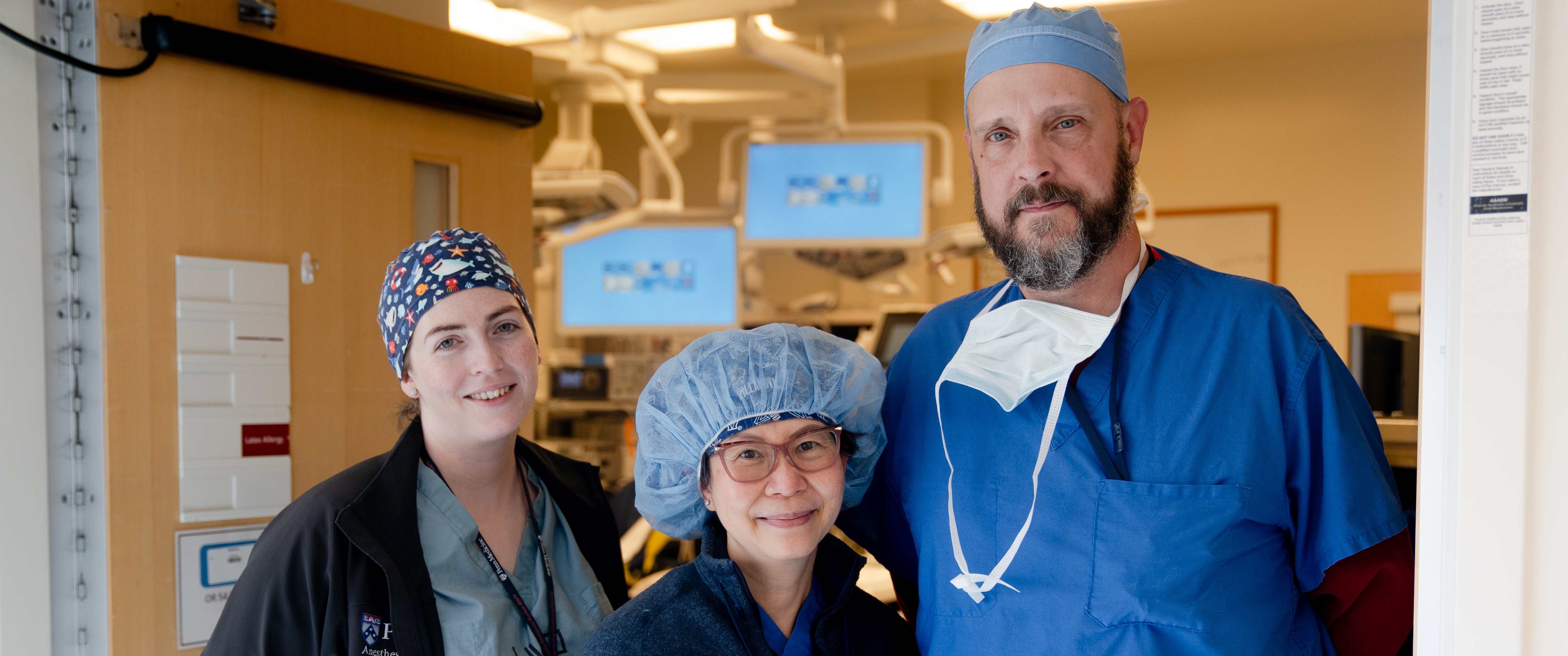 Caoimhe Duffy, Julia Tchou, and Matt Carey stand outside of an operating room