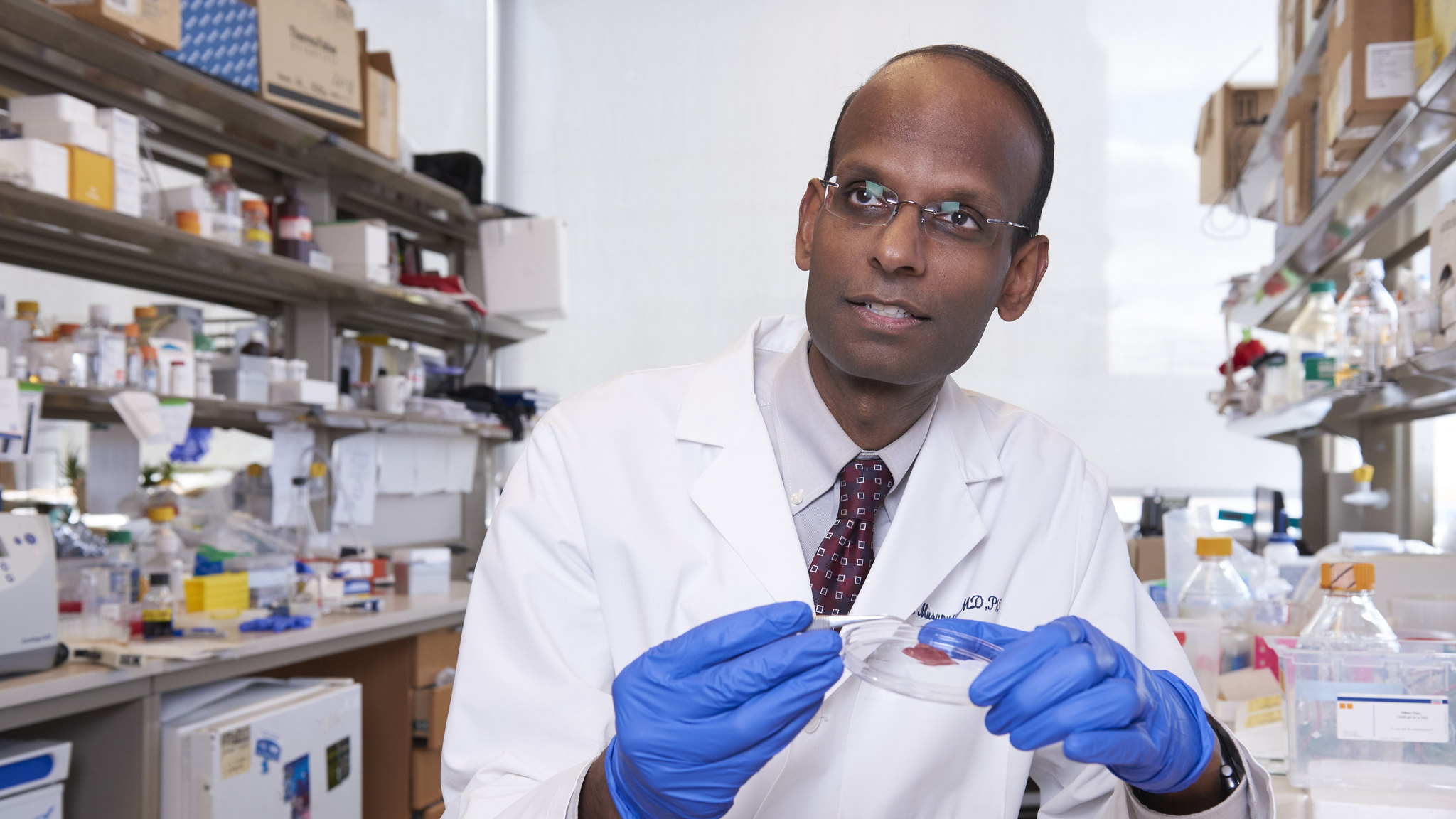 Kiran Musunuru, MD, PhD, in a lab wearing a white coat and holding a petri dish