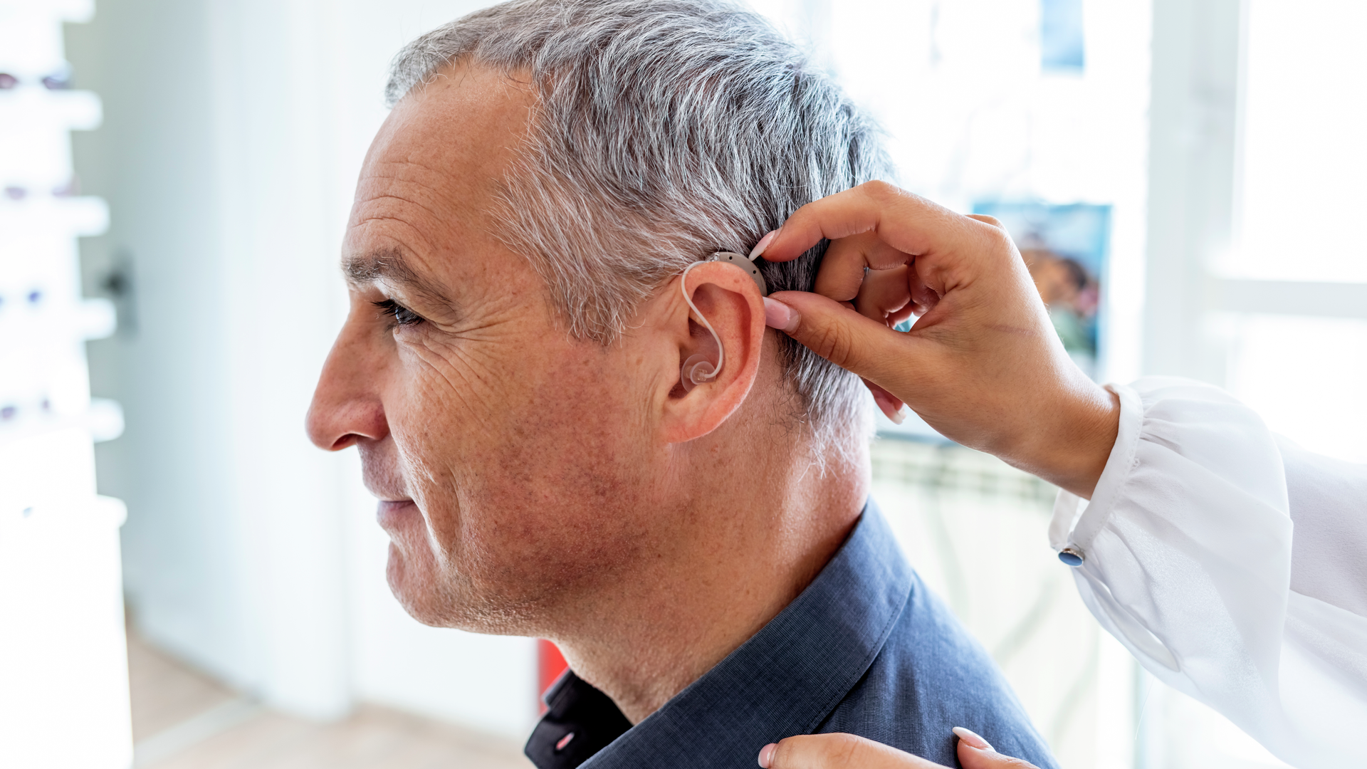 Cropped shot of female doctor inserting hearing aid in man's ear