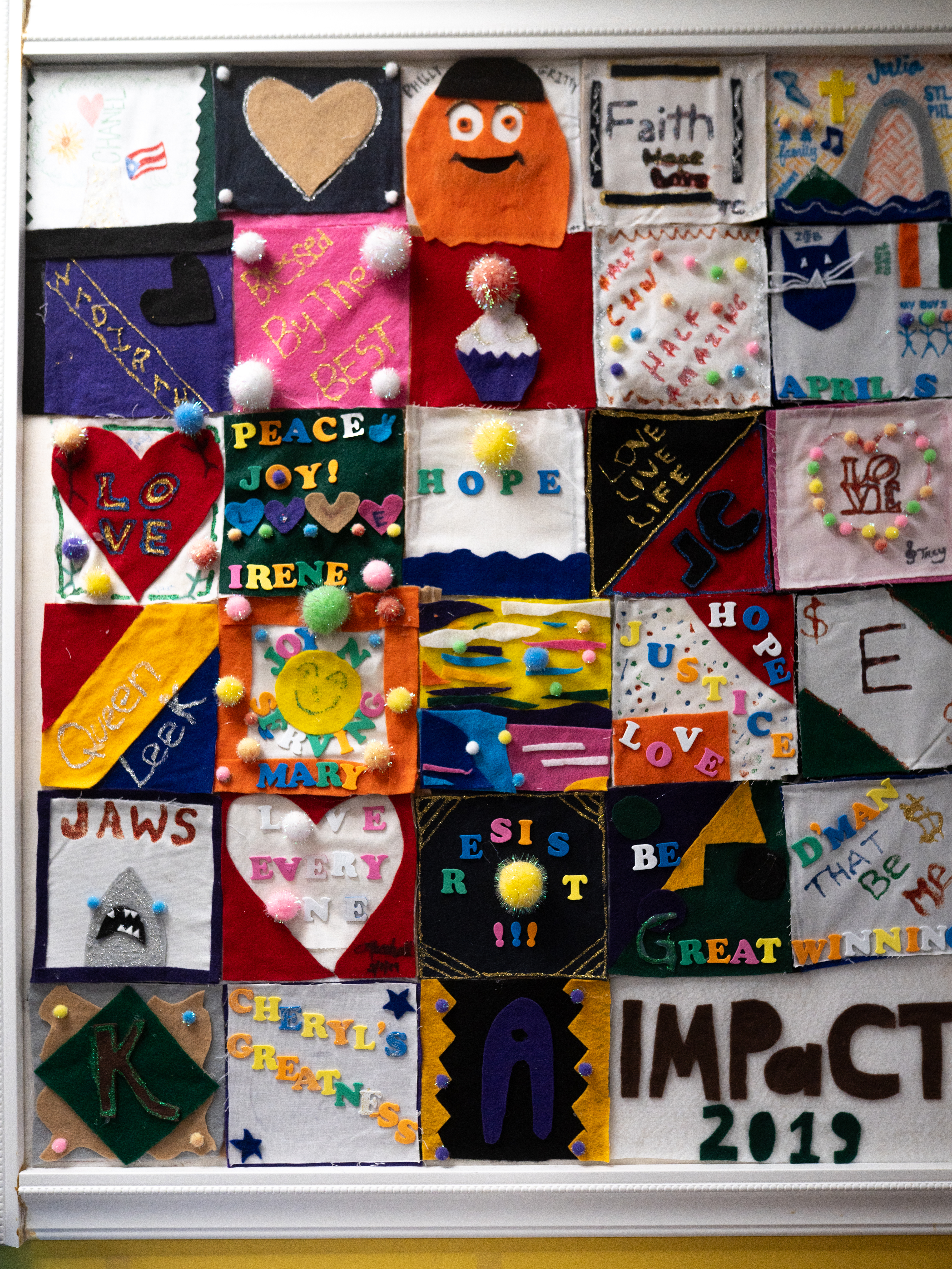 Colorful felt squares featuring words, symbols, and designs including hearts, hope, peace, love and IMPaCT 2019 displayed together on a wall