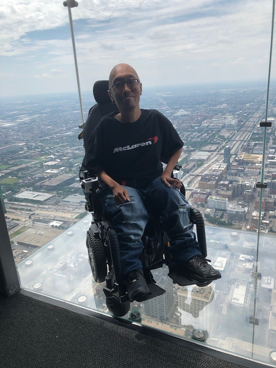 Simon Cantos, seated in a wheelchair on a glass balcony at a high vantage point overlooking Chicago