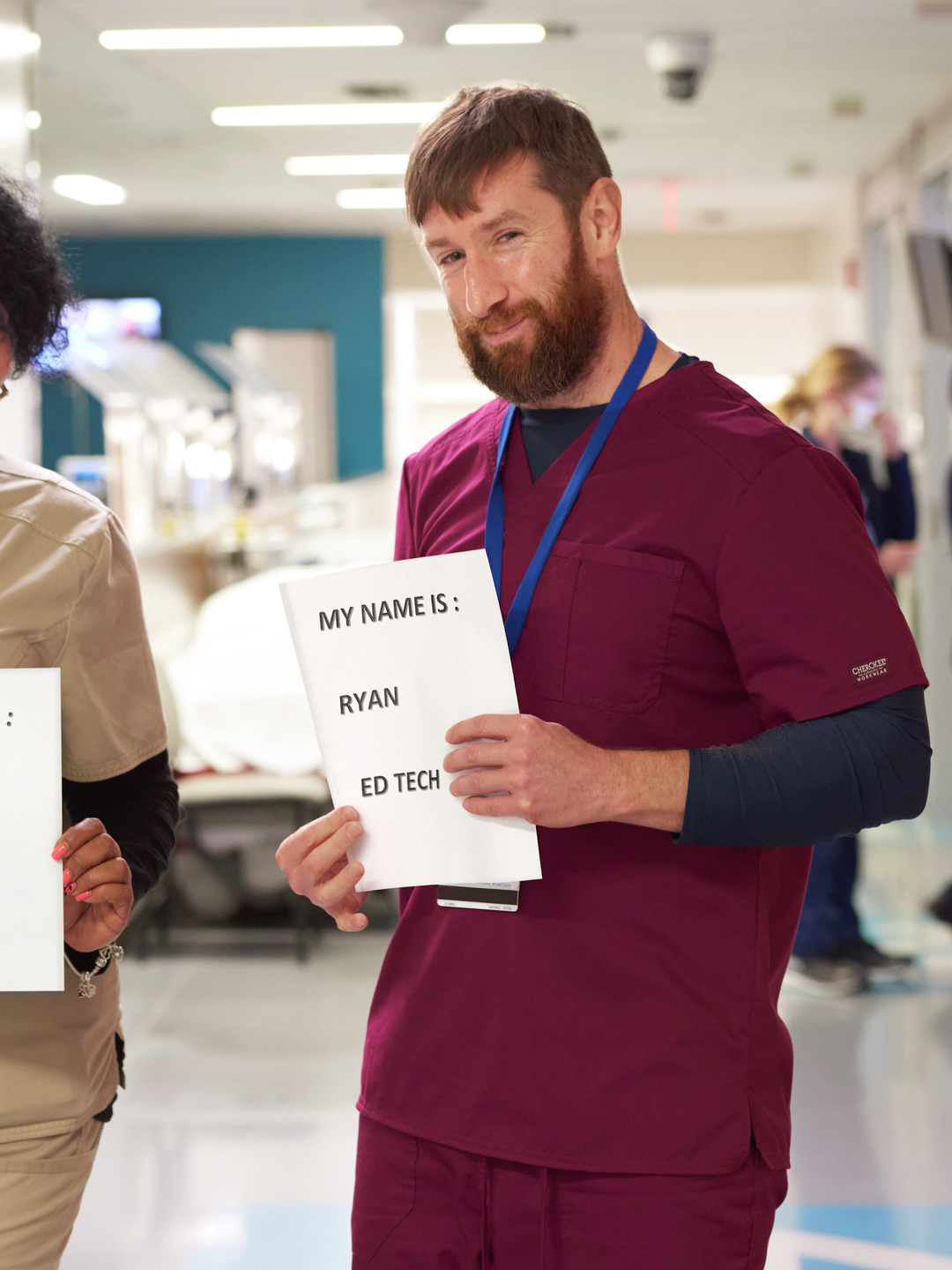 Two staff members hold up pieces of paper displaying their names and job titles