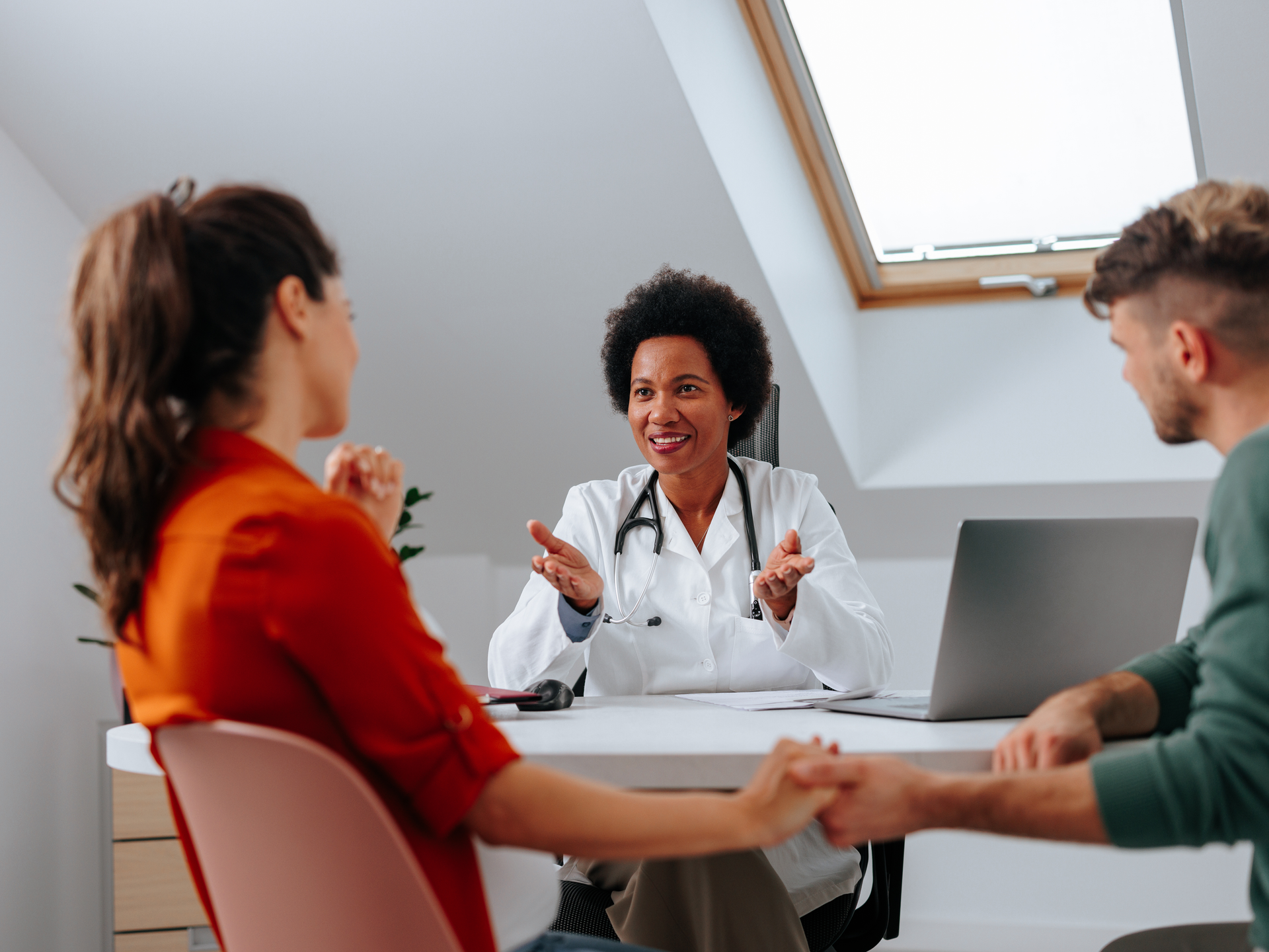 A pregnant woman and her partner holding hands and speaking to a doctor. 