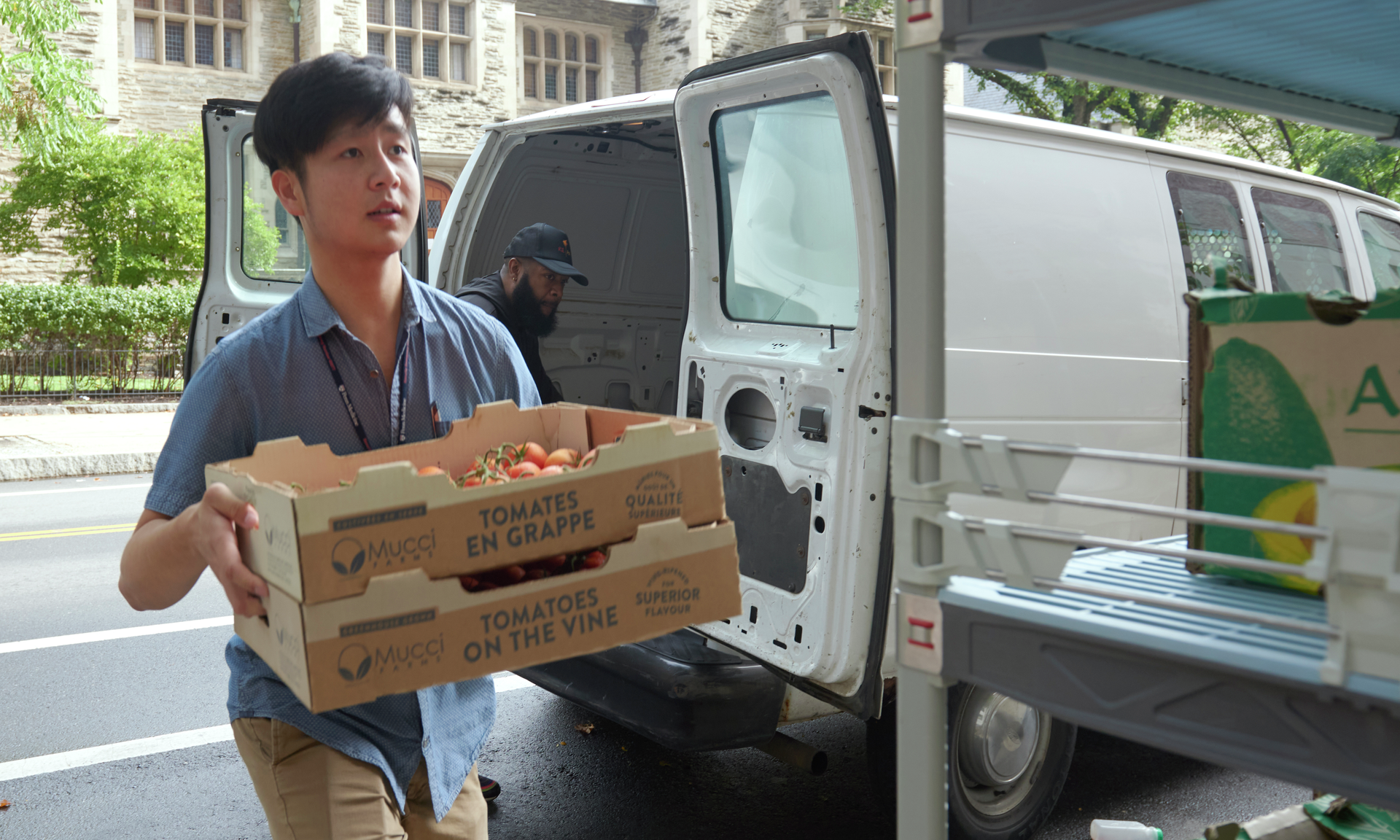 A young man carries a wooden crate of produce from a van toward the hospital