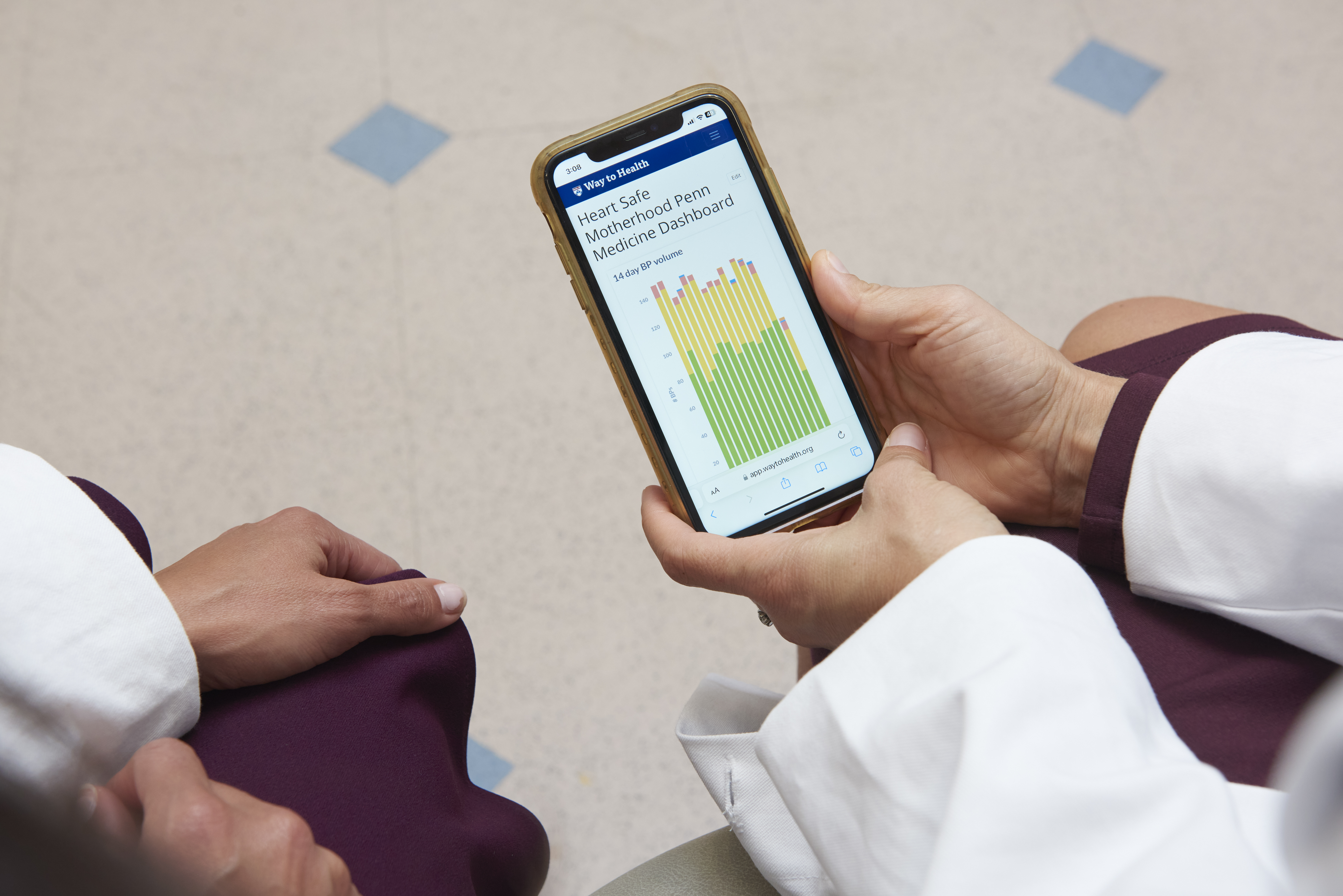 The hands of two female doctors in white coats hold a phone whose screen displays a data chart "Heart Safe Motherhood Dashboard"