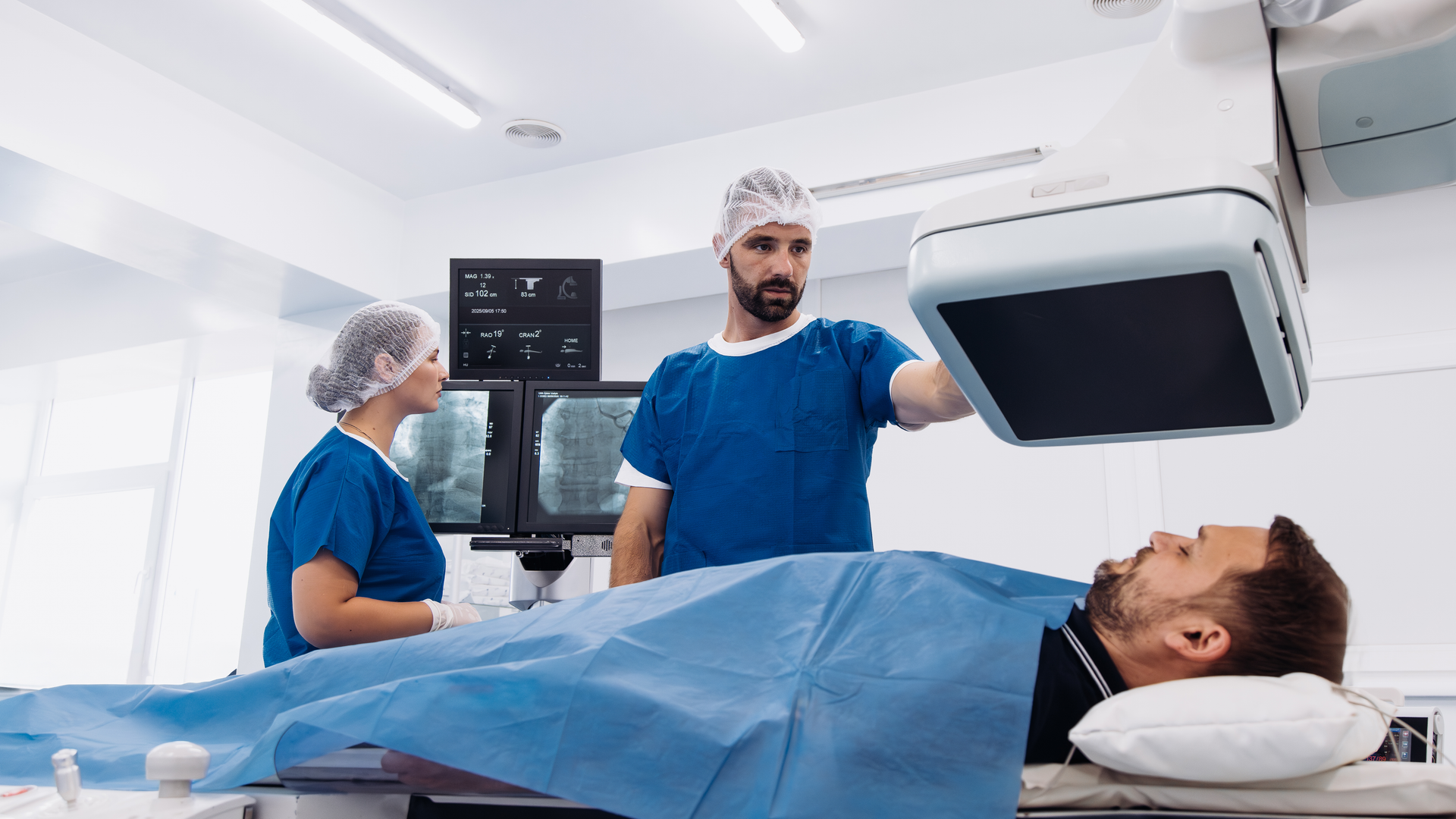 Medical professionals in blue scrubs performing an angiograph procedure on a patient lying on a table, showcasing advanced imaging technology in a modern healthcare environment