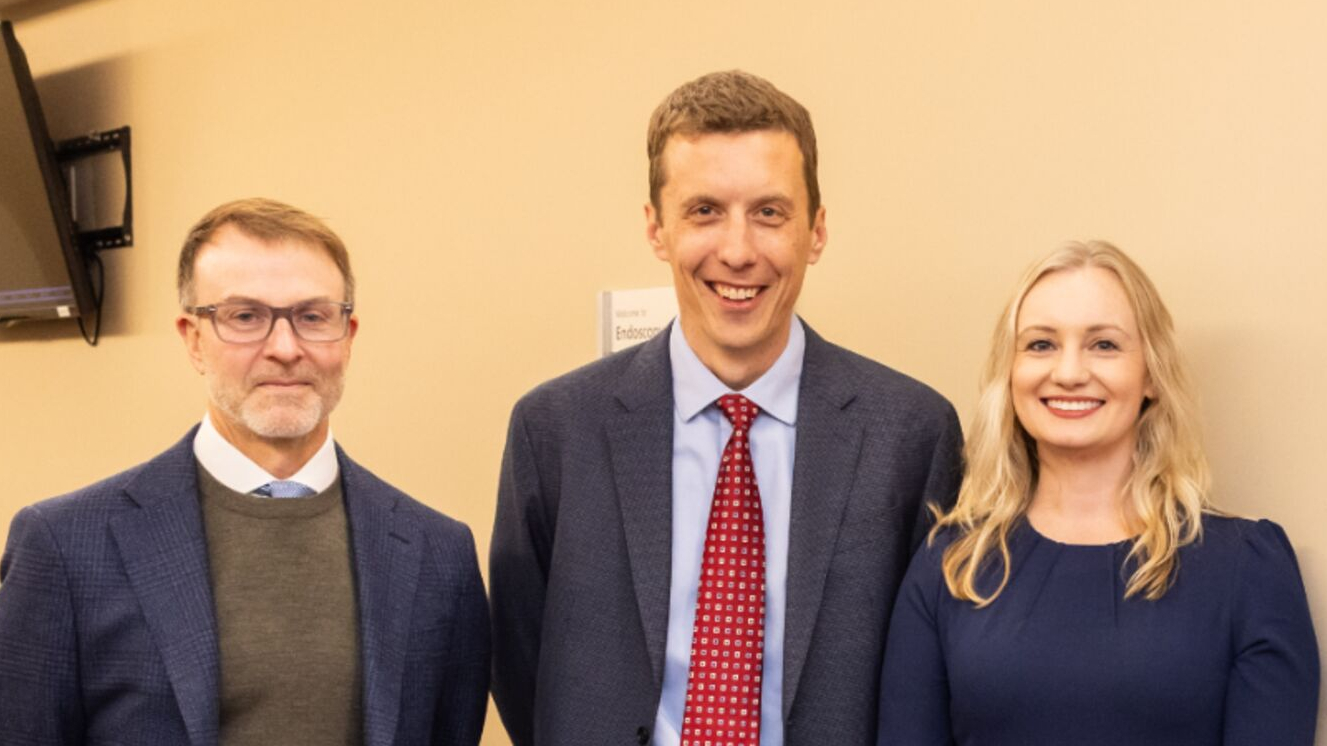 E. John Wherry, Bryson Katona, and Jessica Long standing next to a King Center for Lynch Syndrome sign, MS, CGC