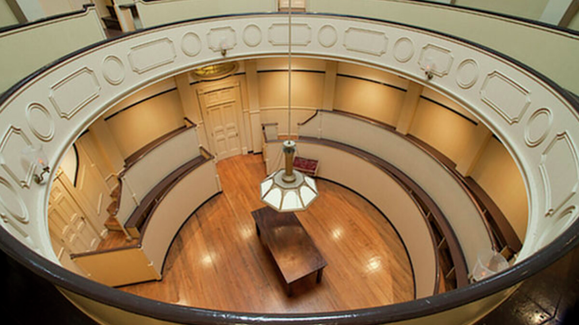 Circular room with steep, tiered wooden seating surrounding a central operating pit, focused on a wooden table. 