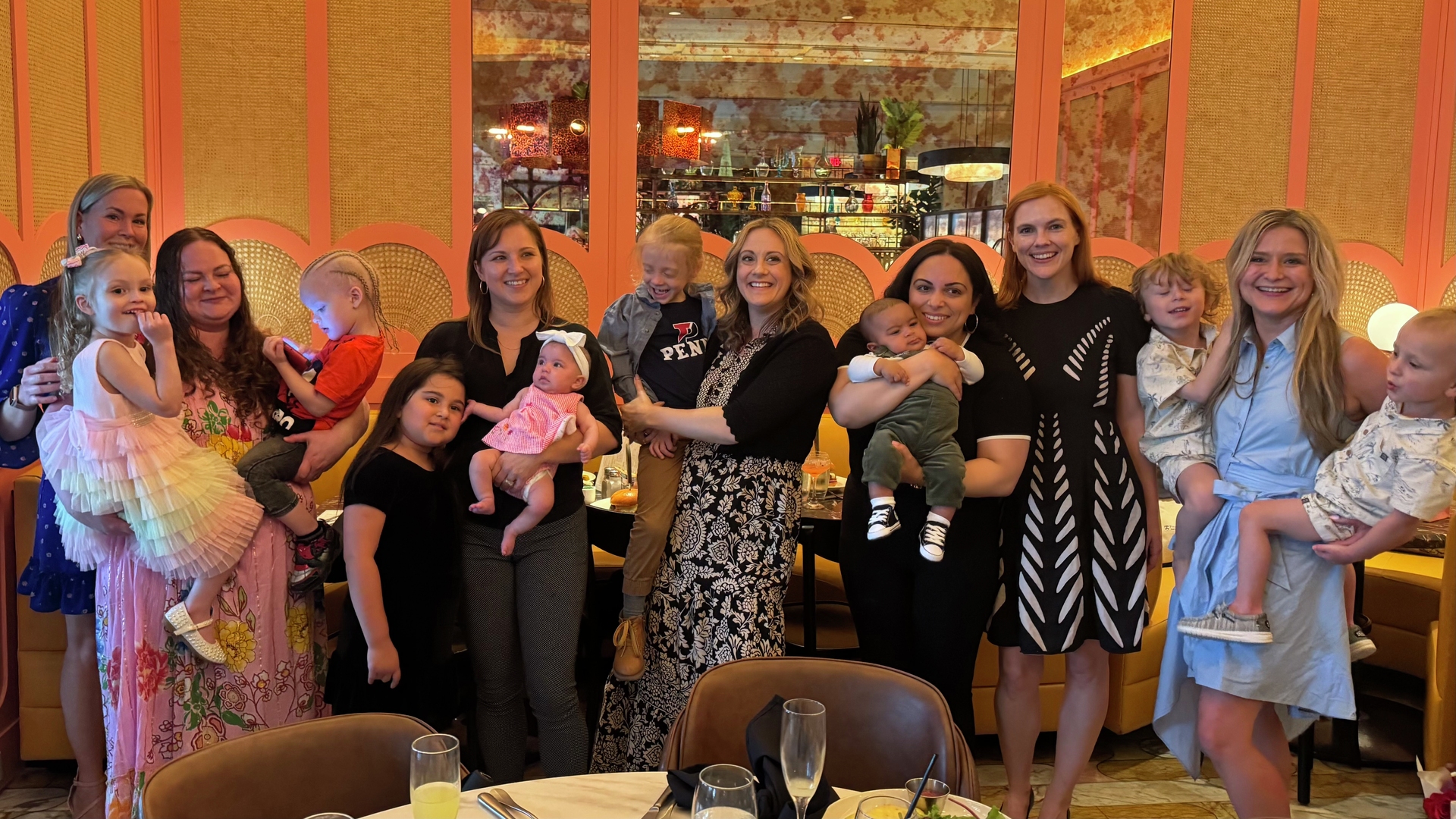 A group of mothers at a restaurant brunch pose for a photo with a gaggle of young children