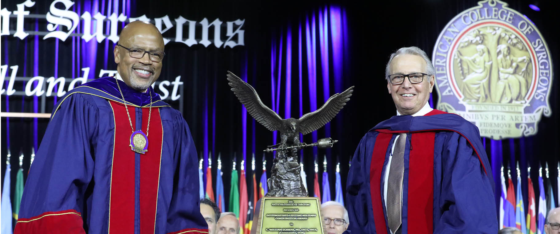 Henri Ford and C. William Schwab, both wearing robes, standing beside an enormous metal award statue of an eagle holding a scepter.