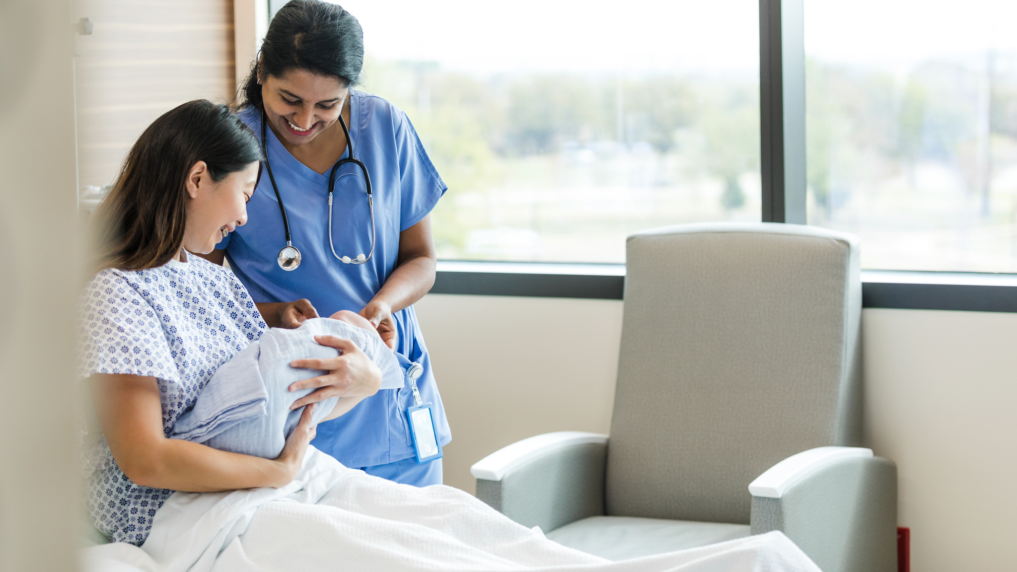 Nurse smiles and admires the baby with the new mother