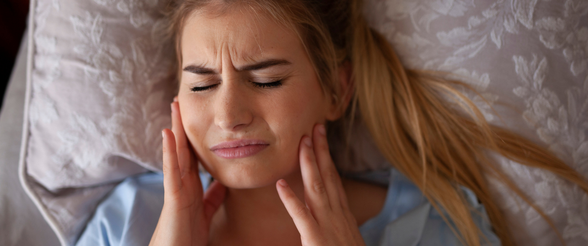 Woman lying on pillow in pain with hands touching jaw