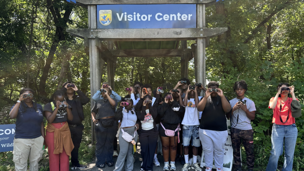 A group of people with binoculars stand in front of the entrance to a U.S. Fish & Wildlife Service visitor center