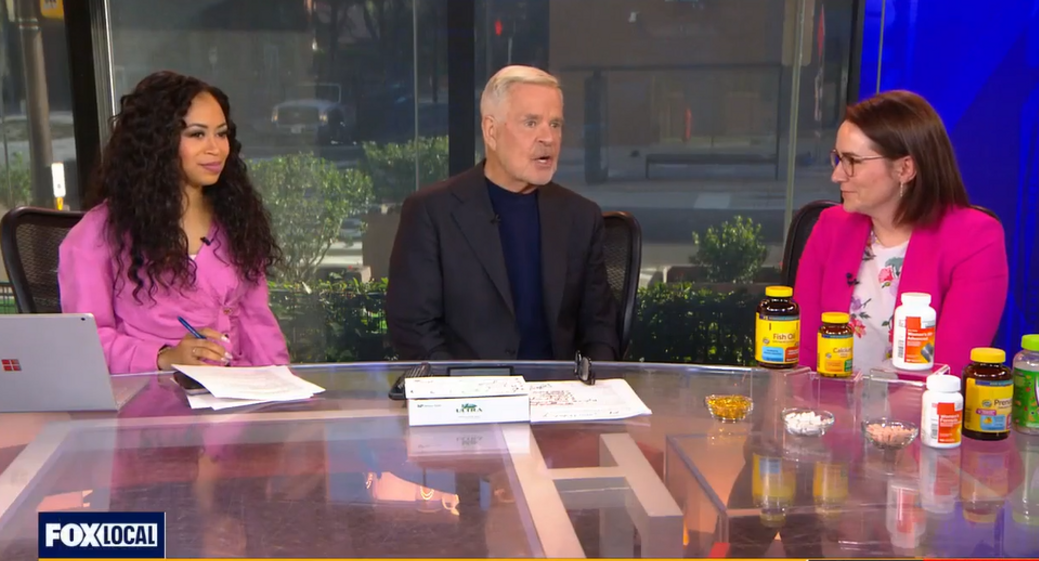 Colleen Tewksbury at a news desk, with bottles of supplements on its surface, and speaking with FOX29 anchors