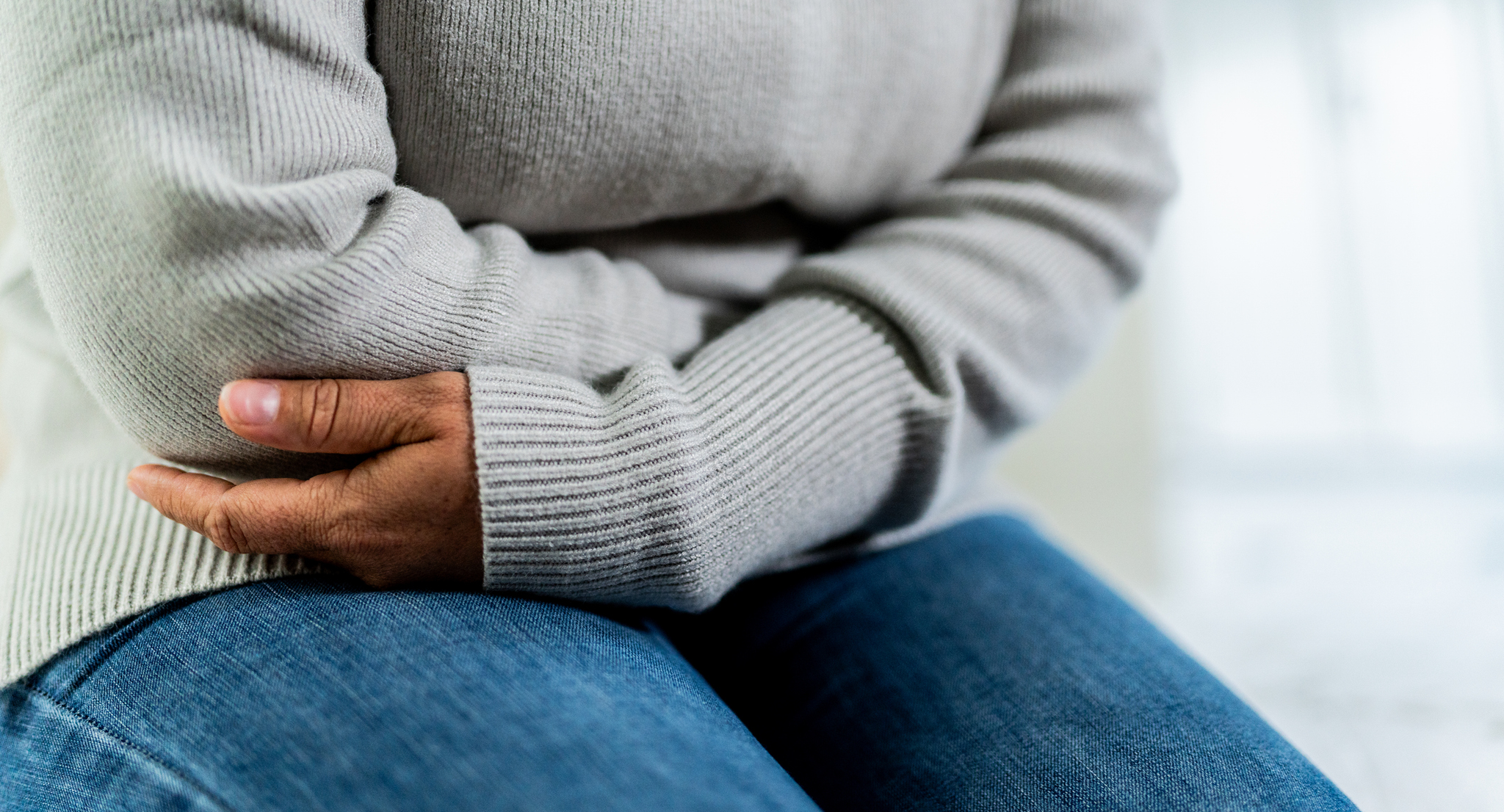 A woman with her arms crossed over her stomach, indicating pain