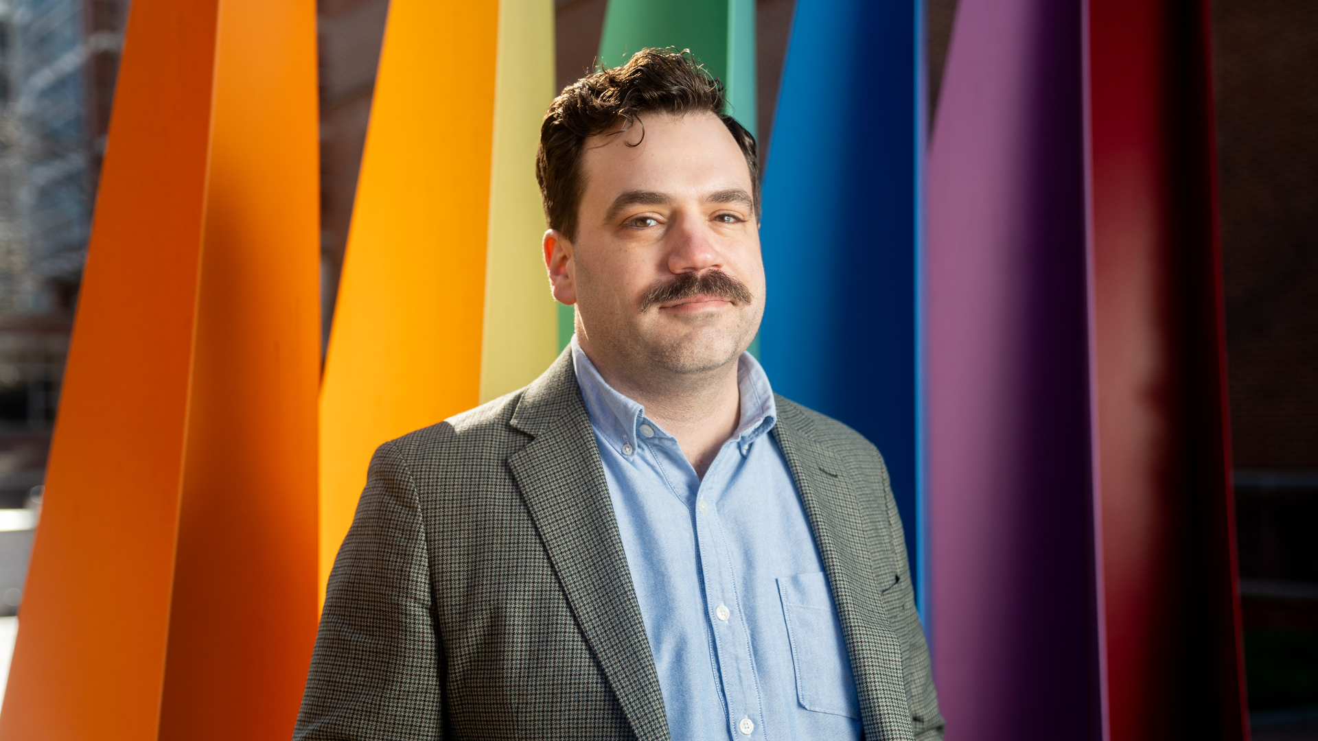 Kevin Kline, MD, stands in front of an abstract art installation representing the rainbow pride flag.