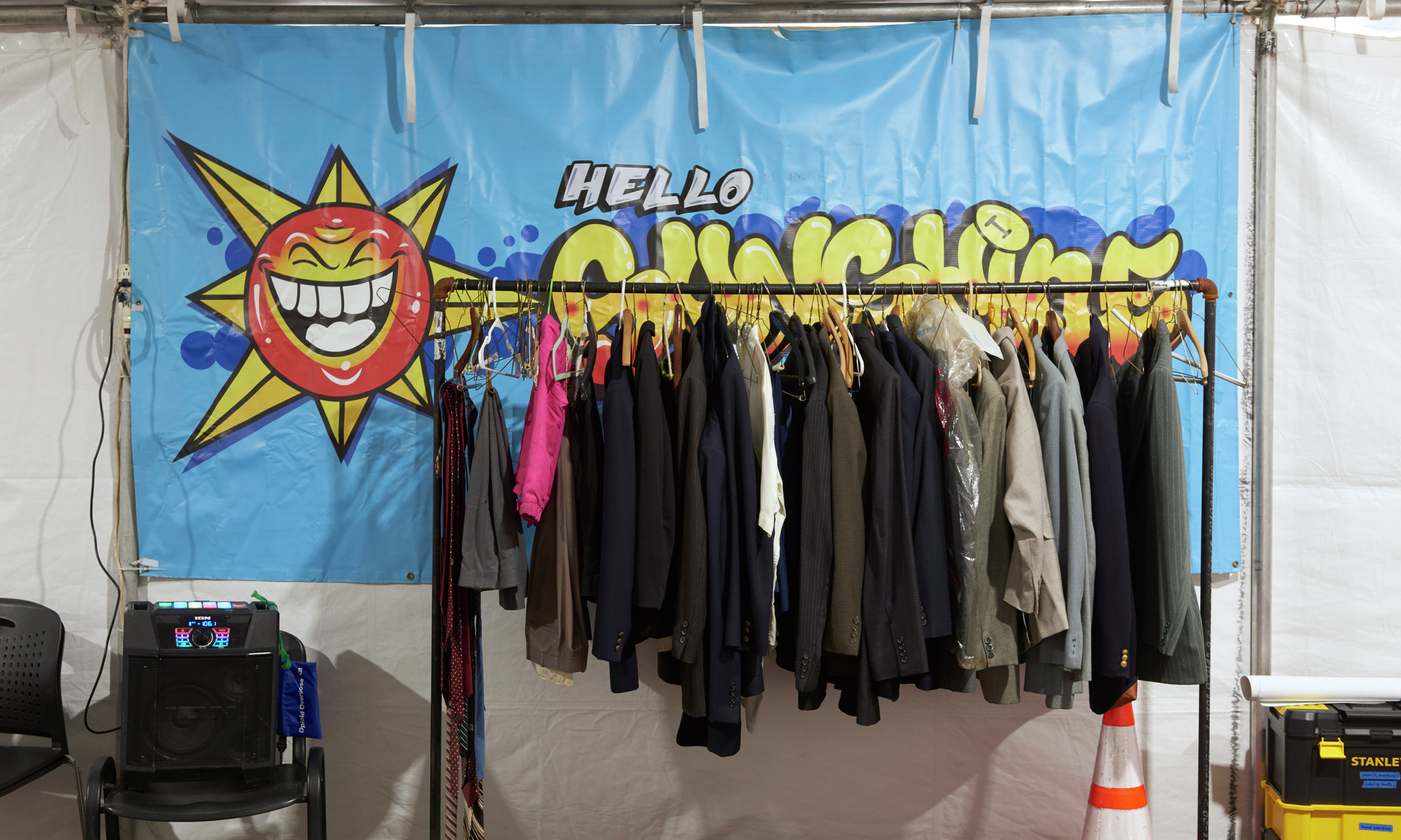 A rack full of free clothing is in front of a large banner that says "Hello Sunshine"