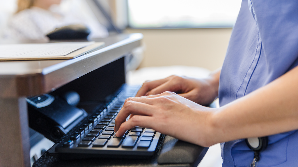 Healthcare worker's hands typing on a computer keyboard