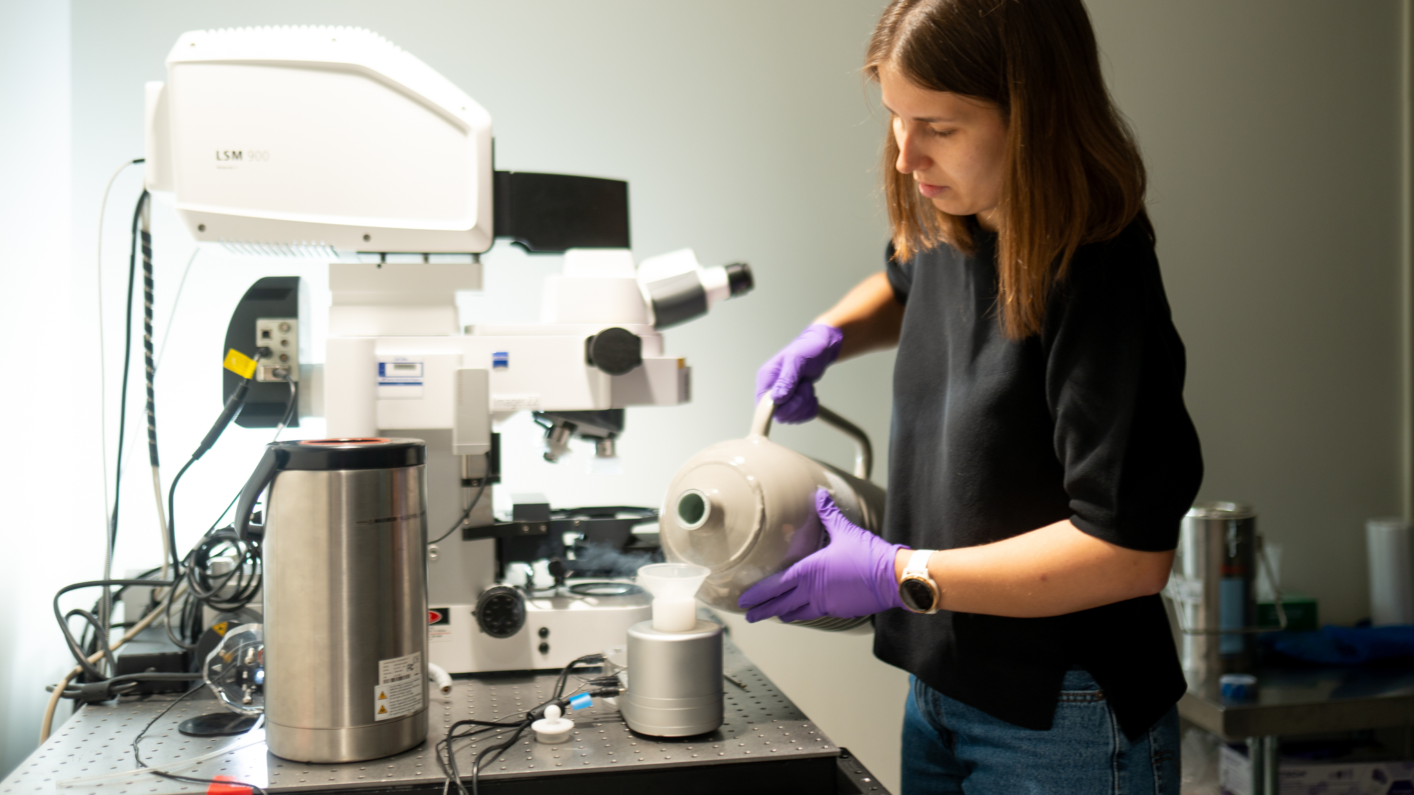 Standing next to a microscope, Kathryn Kixmoeller pours liquid nitrogen from a jug into a small sample container