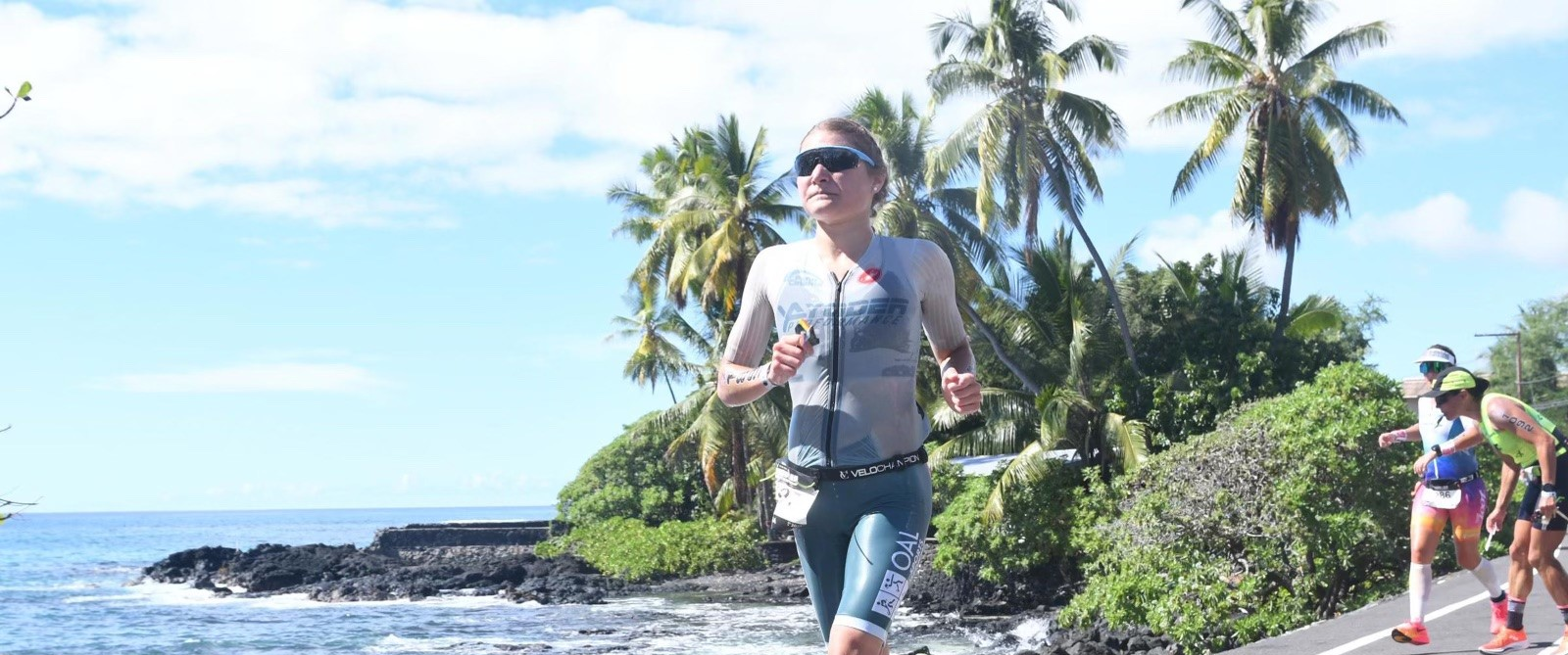 Ava Warfel, dressed in running gear, runs on a road alongside an ocean coastline