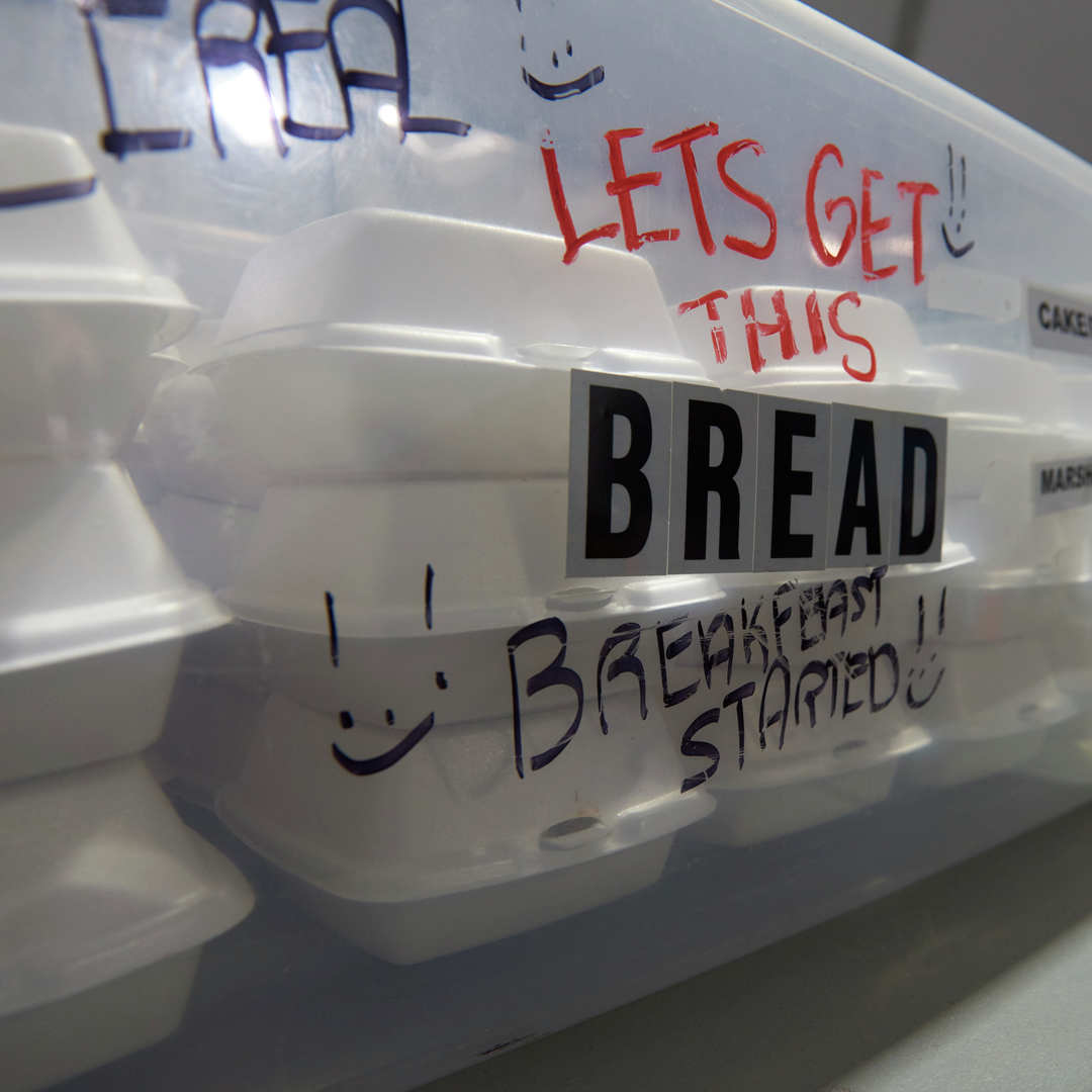 A plastic bin filled with take-out containers of food is labeled "Let's get this Breakfast Started" with smiley faces