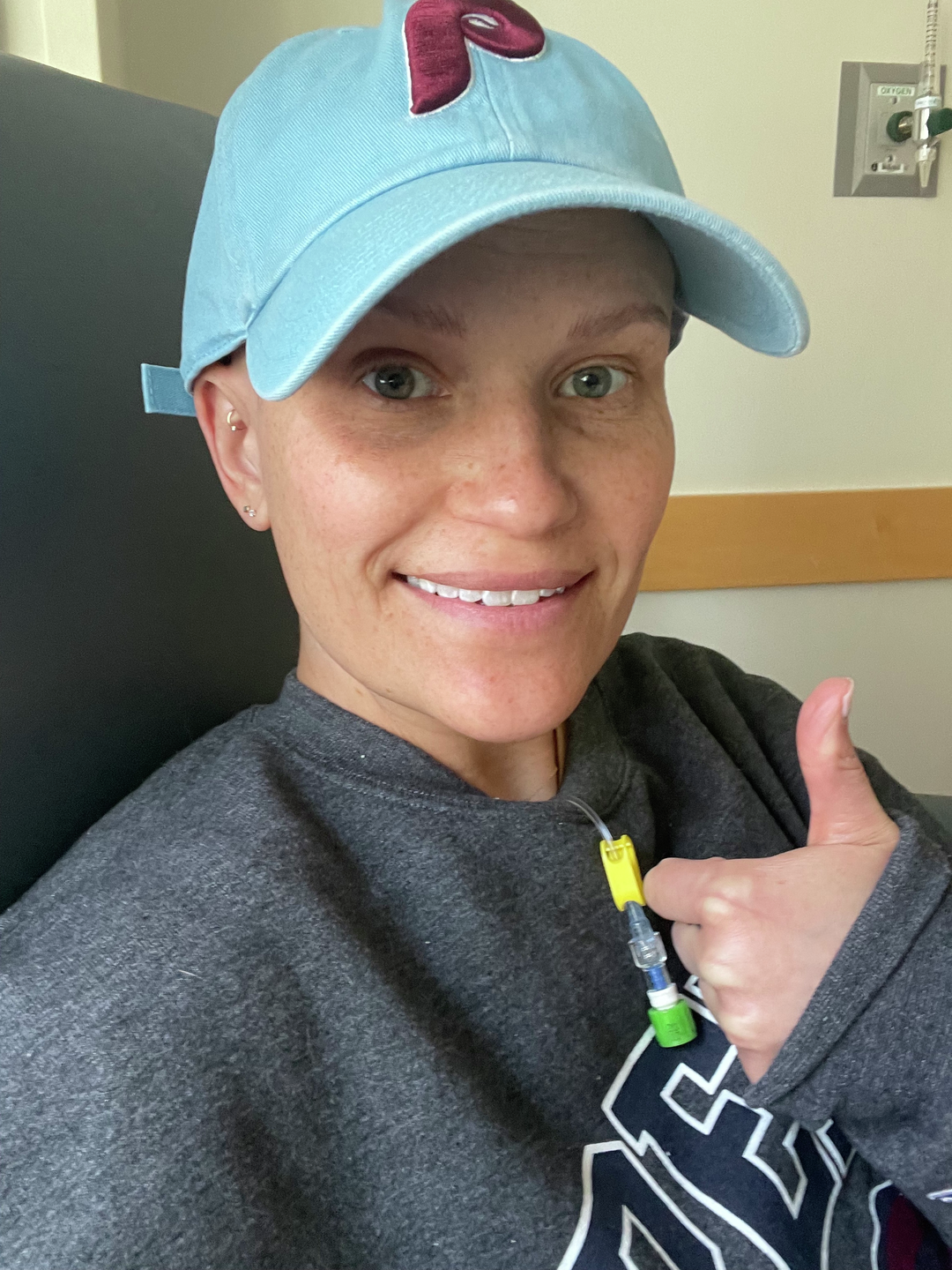 Kate Korson, with a bald head in a Phillies baseball cap, gives a thumbs up