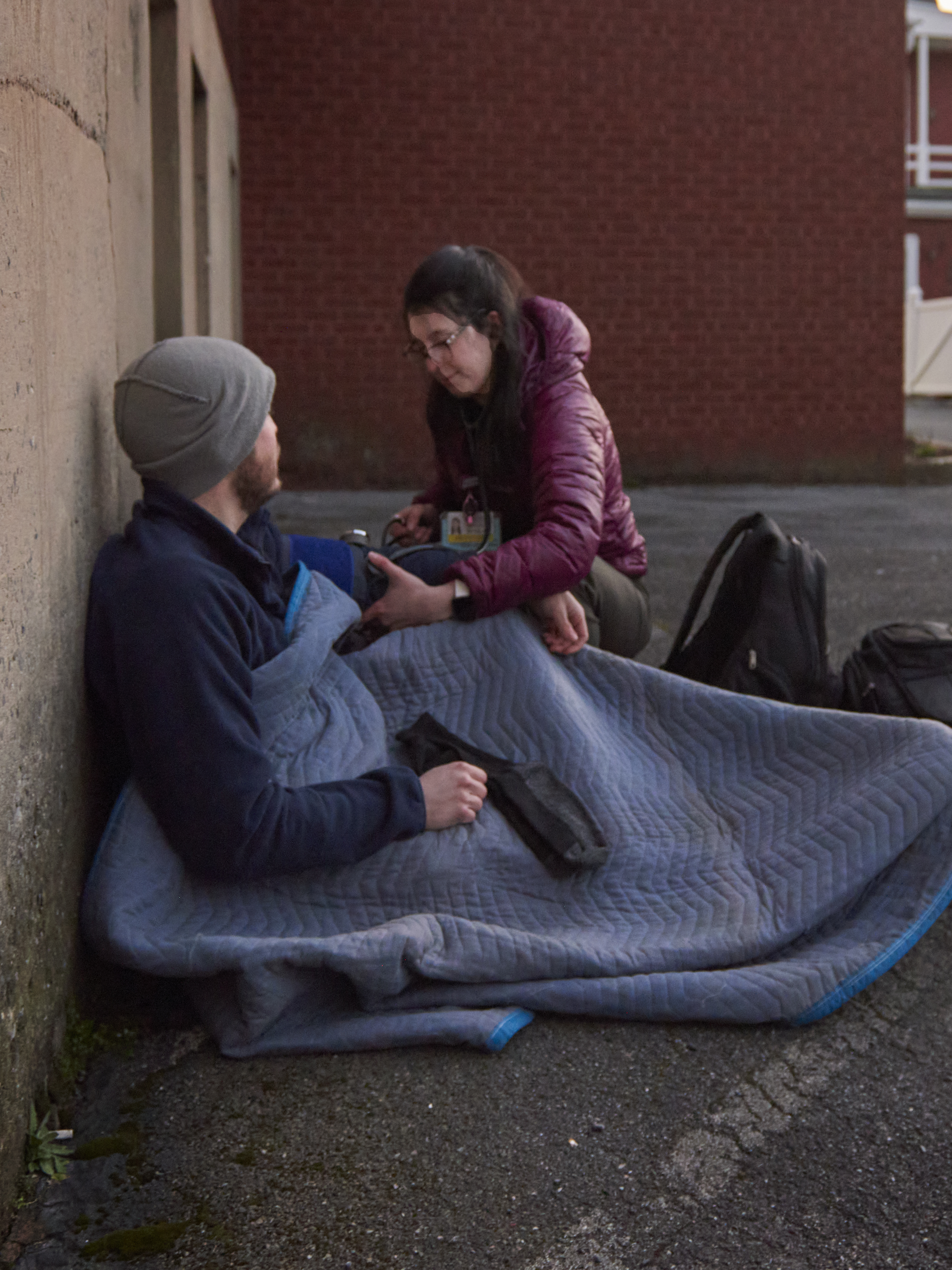 Samantha Bush, DO, takes a blood pressure reading from a man lying under a blanket in a parking lot