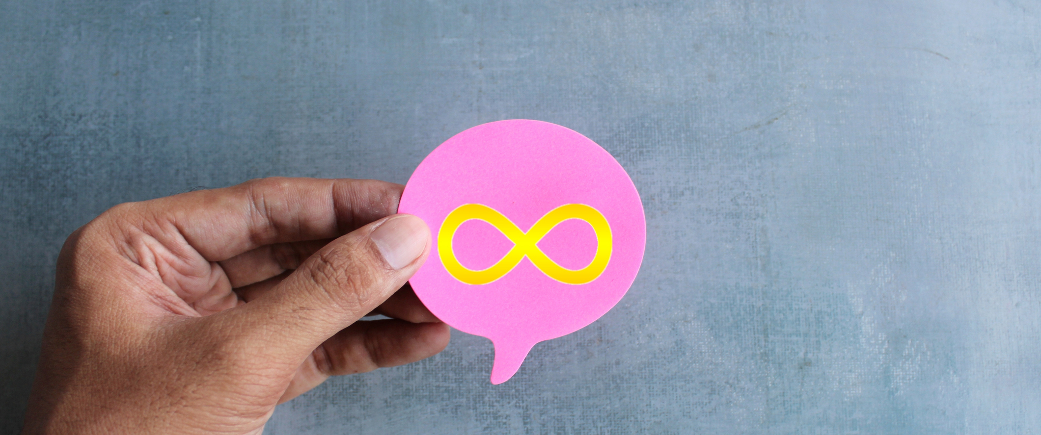 A hand holding a speech bubble with a gold infinity symbol in its center