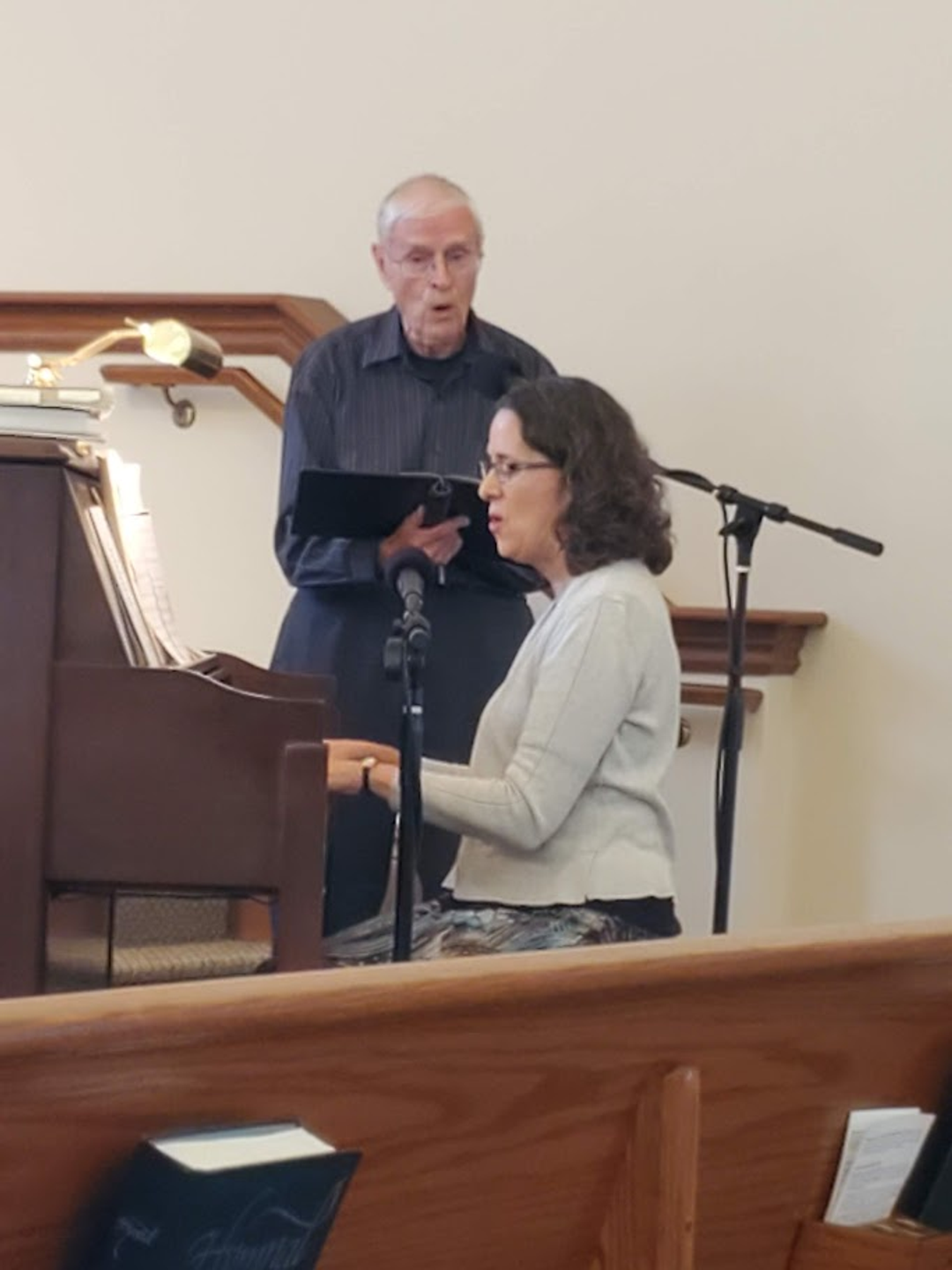 Dick Boshart singing next to a woman playing the piano.