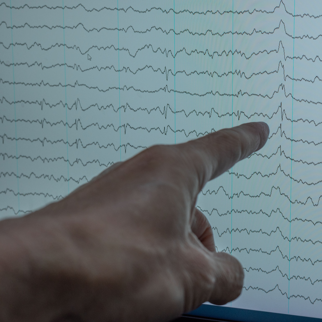 A hand pointing at EEG graph on screen, analyzing brainwave patterns