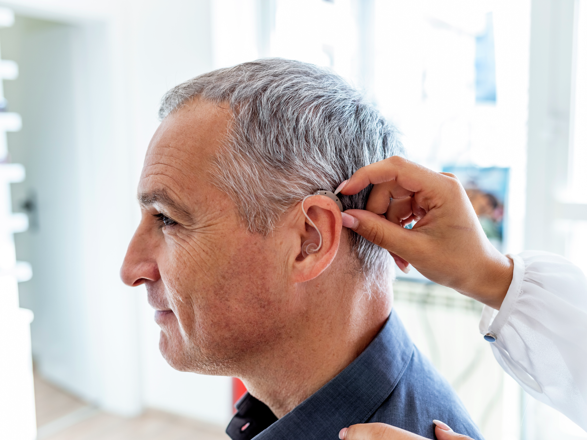 Cropped shot of female doctor inserting hearing aid in man's ear