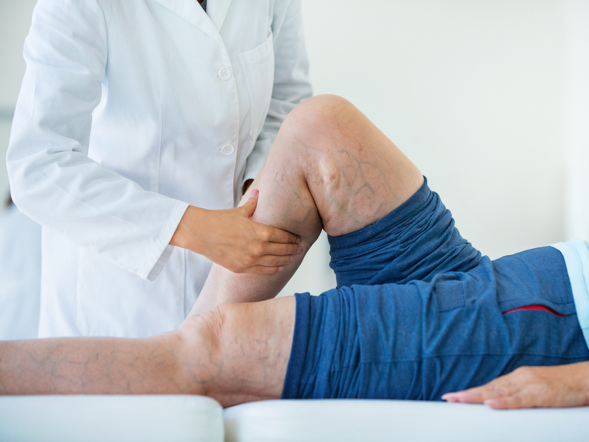 Closeup side view of unrecognizable female doctor massaging legs and calves of a senior female patient with visible varicose veins
